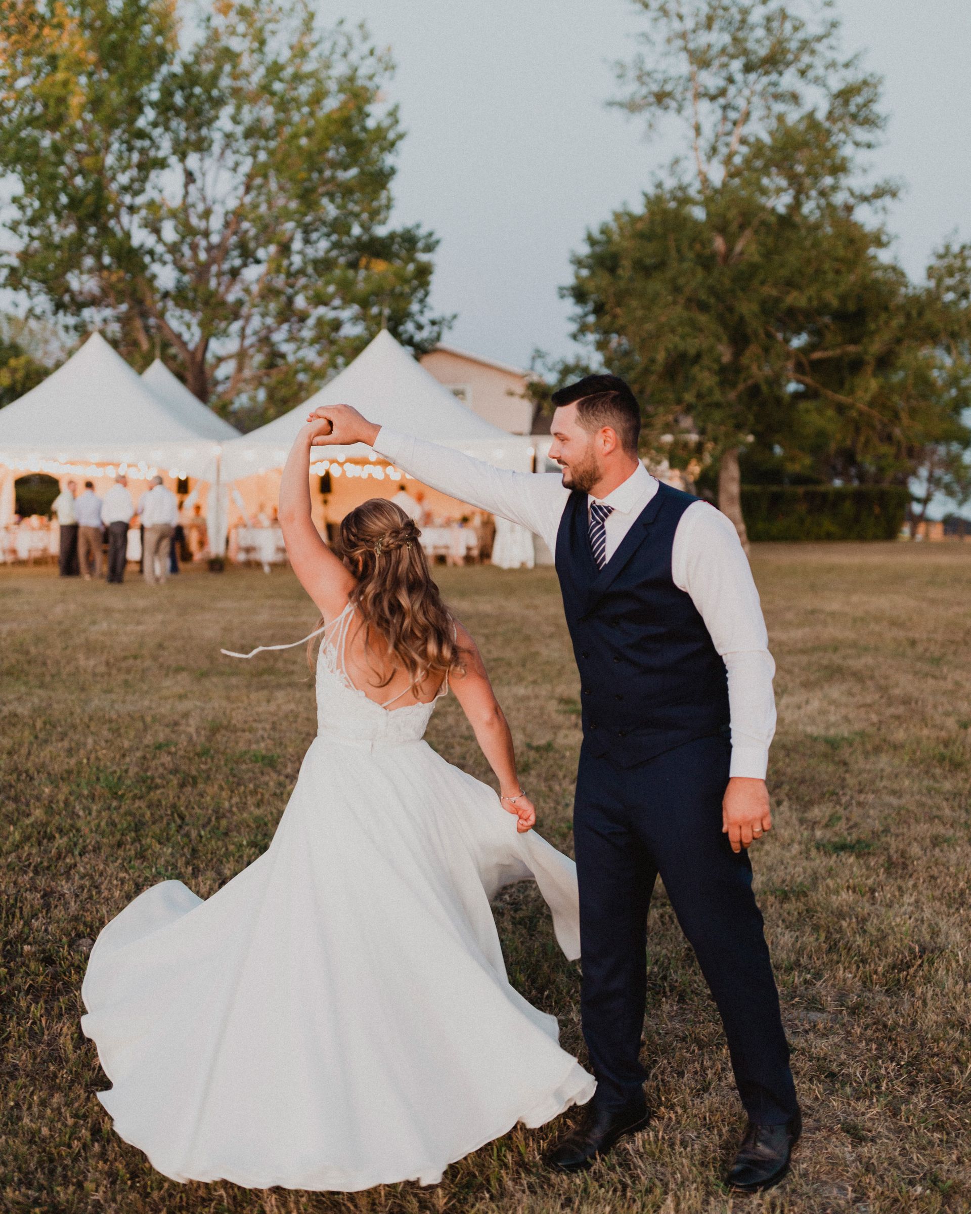 A bride and groom are dancing in a field with tents in the background.