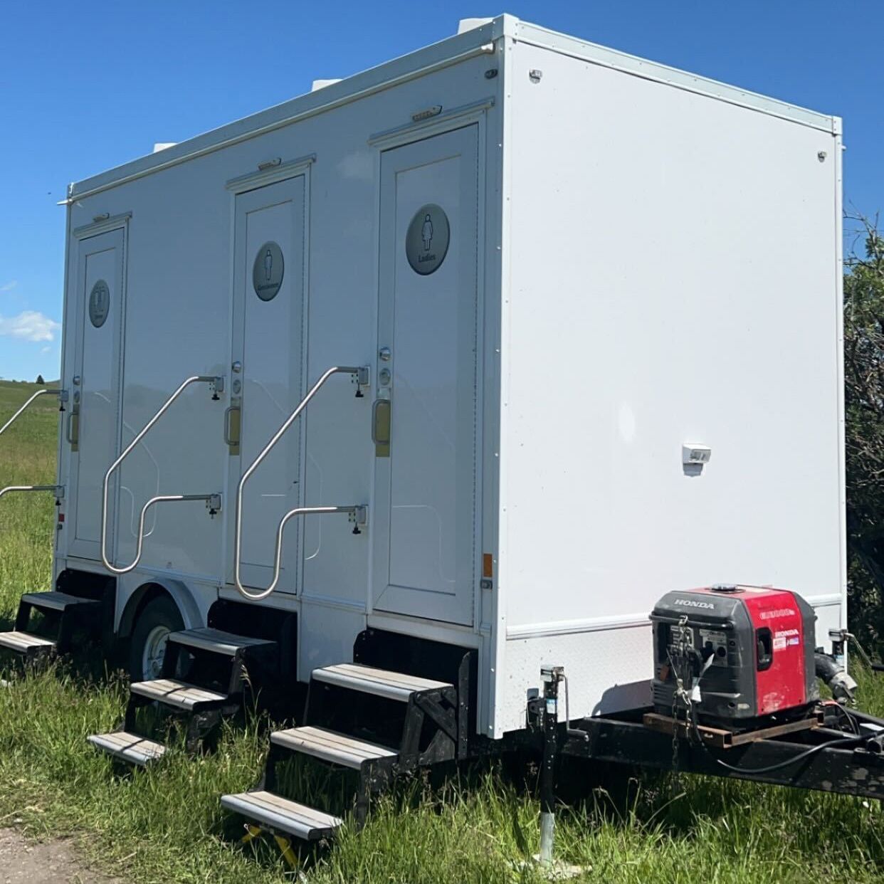 A white trailer with stairs is parked in a grassy field.