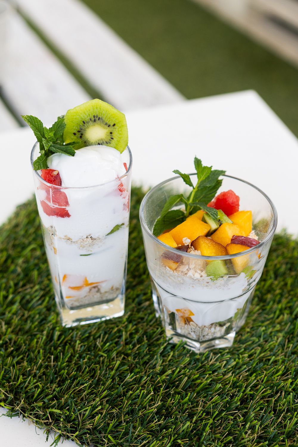 Due bicchieri di yogurt e frutta sono appoggiati su un tavolo.