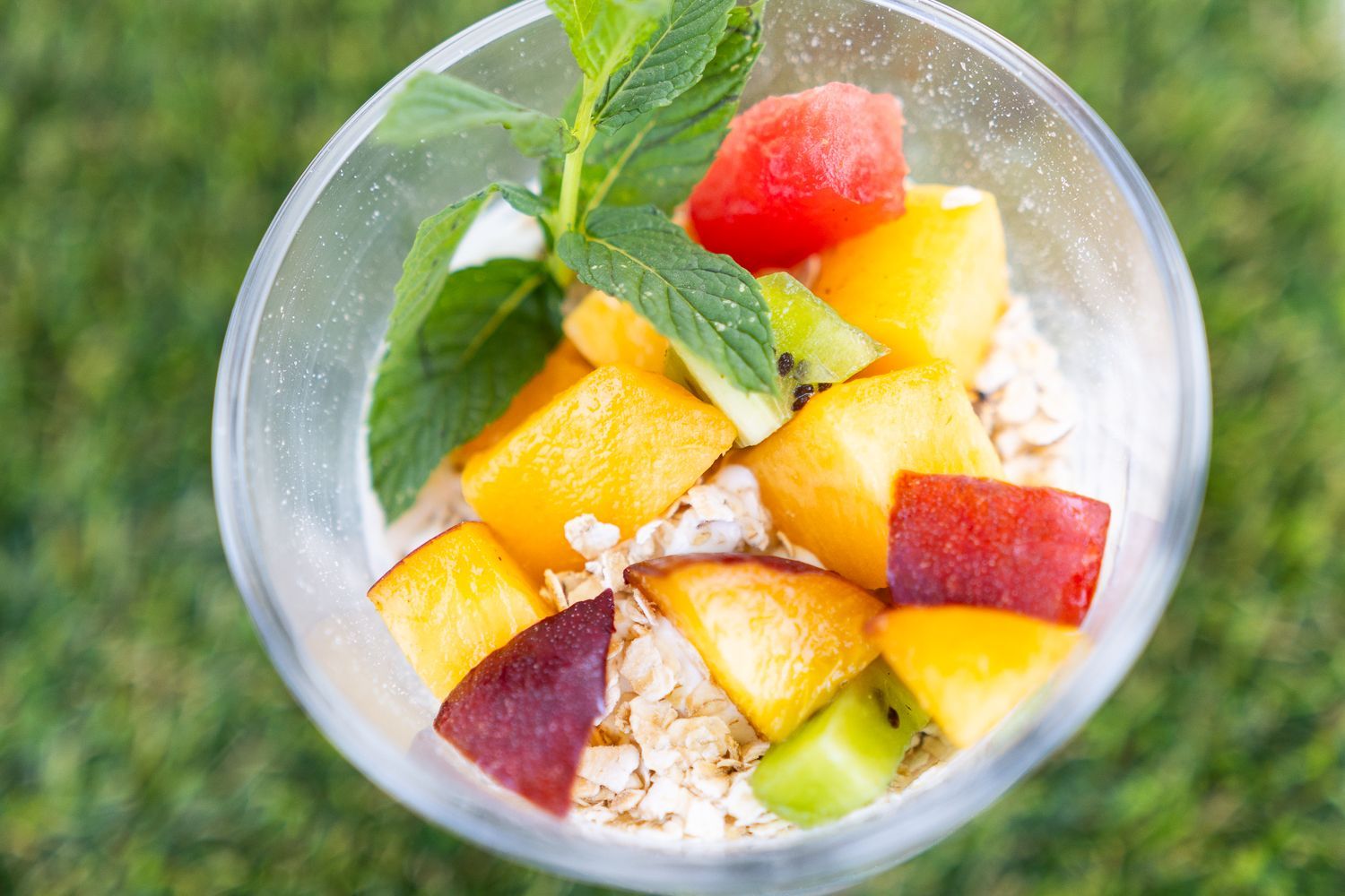 Un bicchiere pieno di fiocchi d'avena, frutta e foglie di menta.