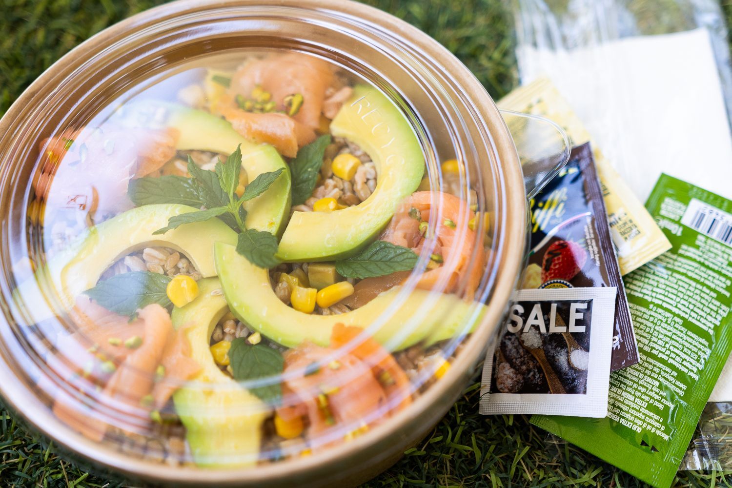 Una ciotola di insalata con avocado, pomodori, mais e altre verdure in un contenitore di plastica.