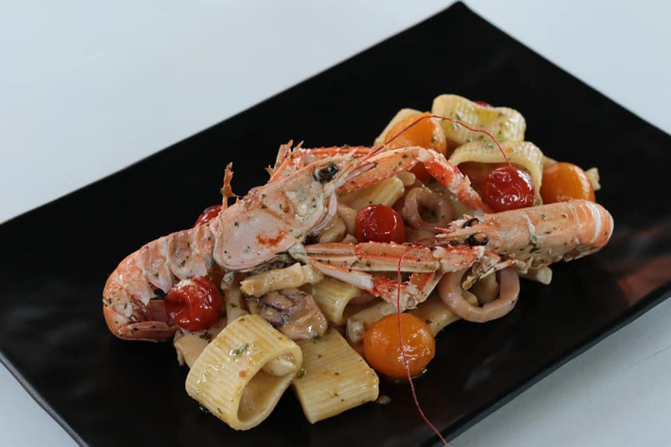 Un piatto nero condito con pasta, gamberi e pomodori