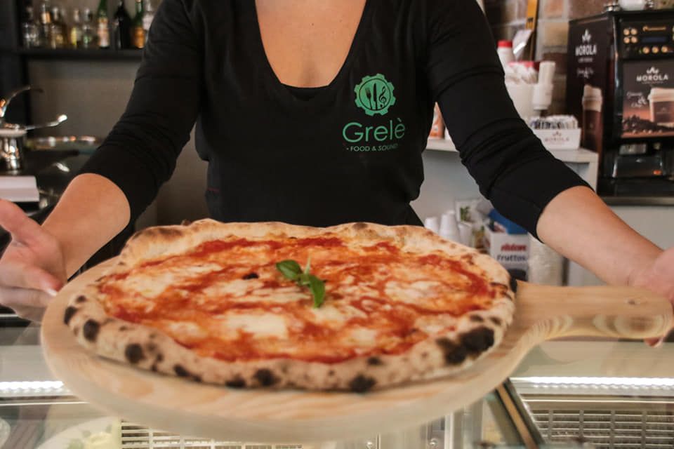 Una donna con una maglietta grele tiene in mano una pizza