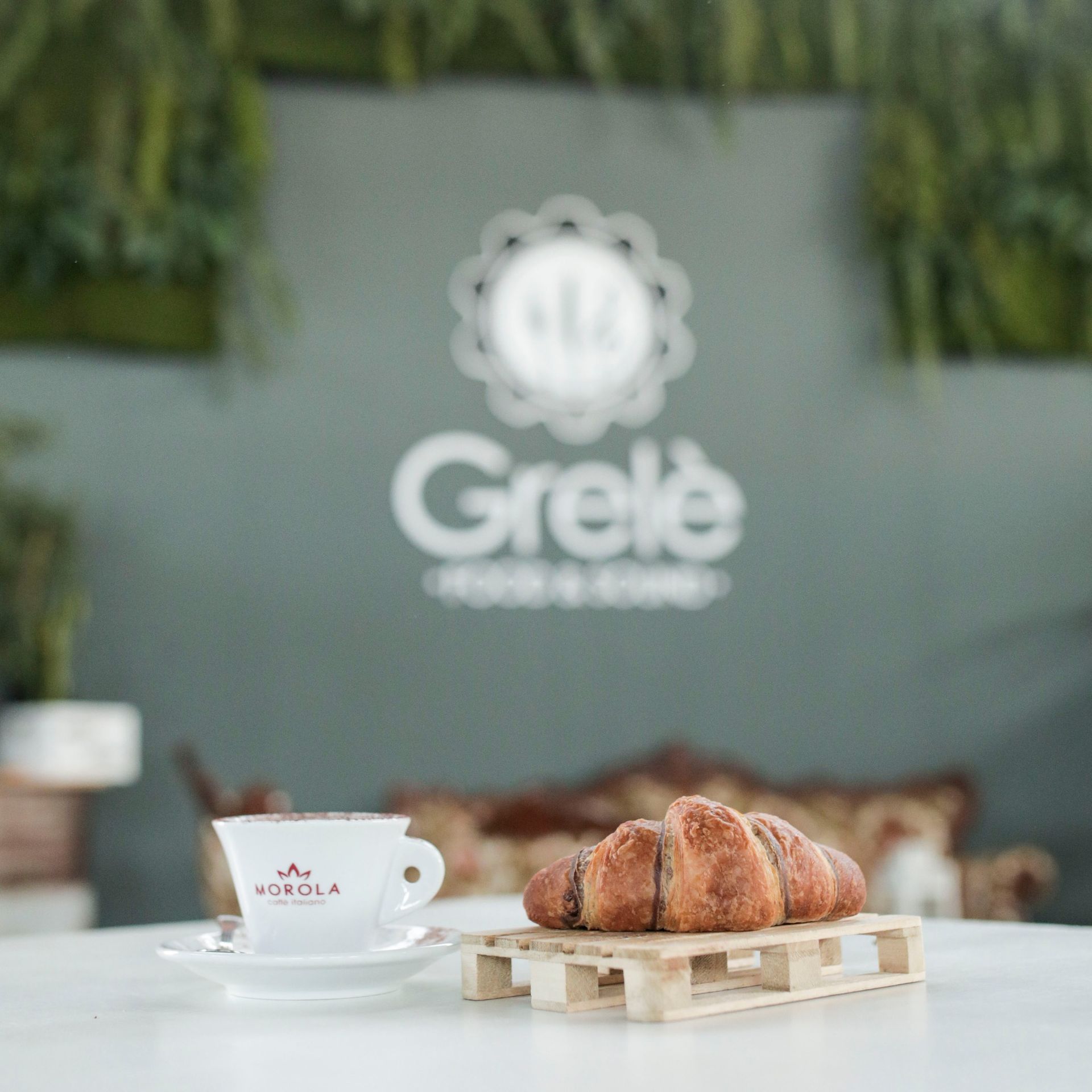 Una tazza di caffè e un croissant su un tavolo davanti a un muro con la scritta grele