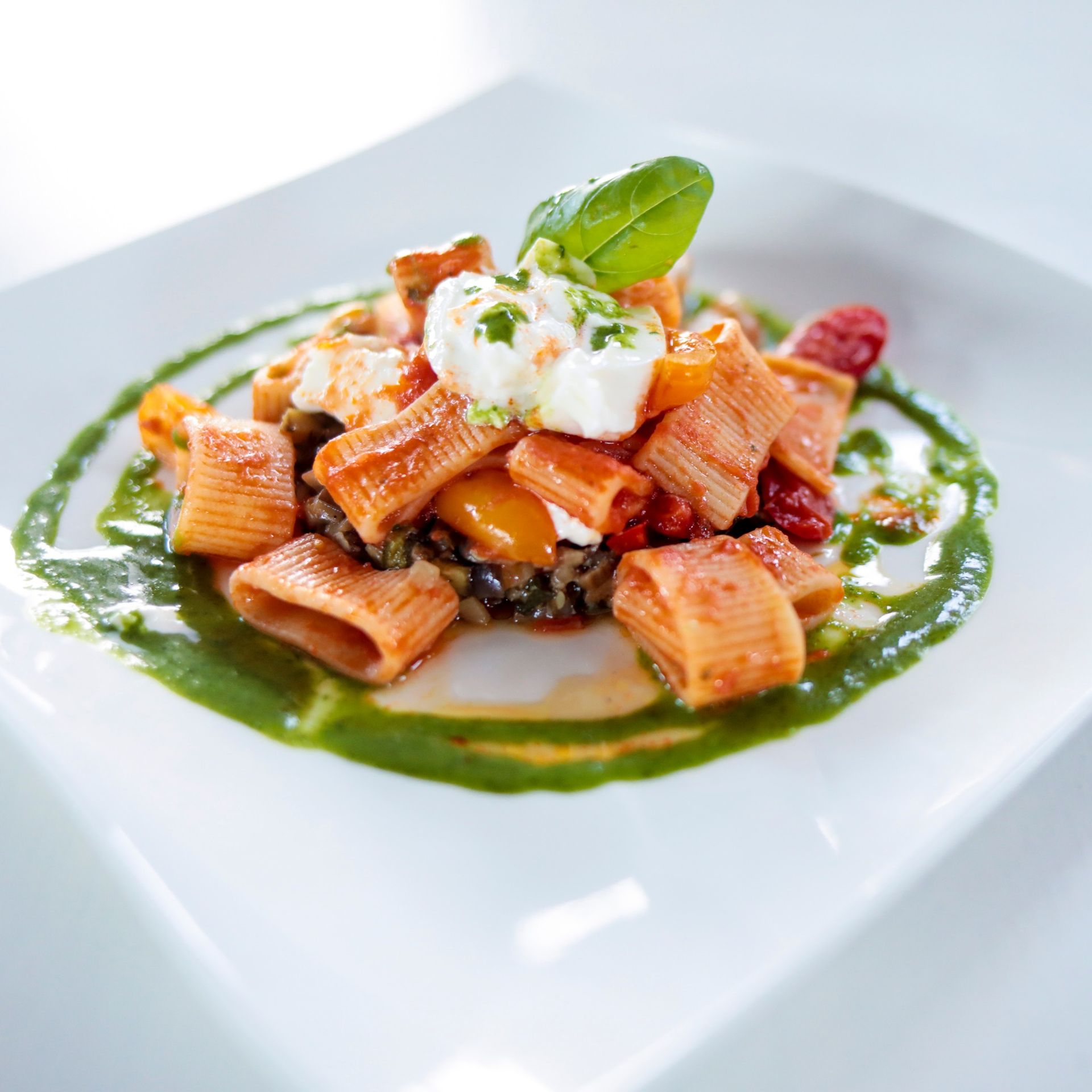 Un piatto bianco condito con pasta e verdure con salsa verde