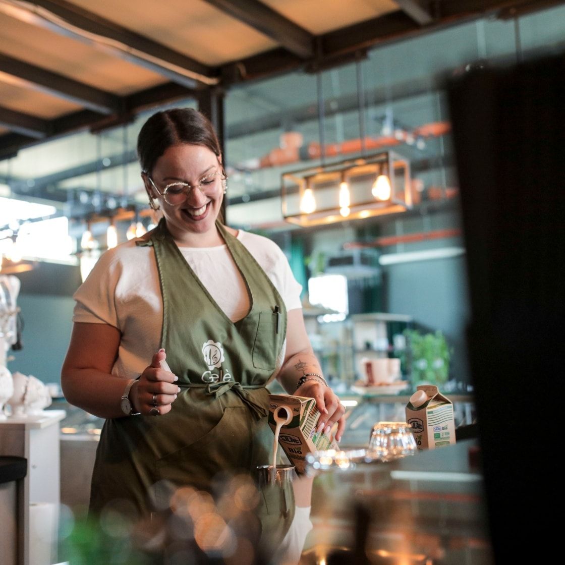Una donna con un grembiule versa il latte in un bicchiere in cucina.