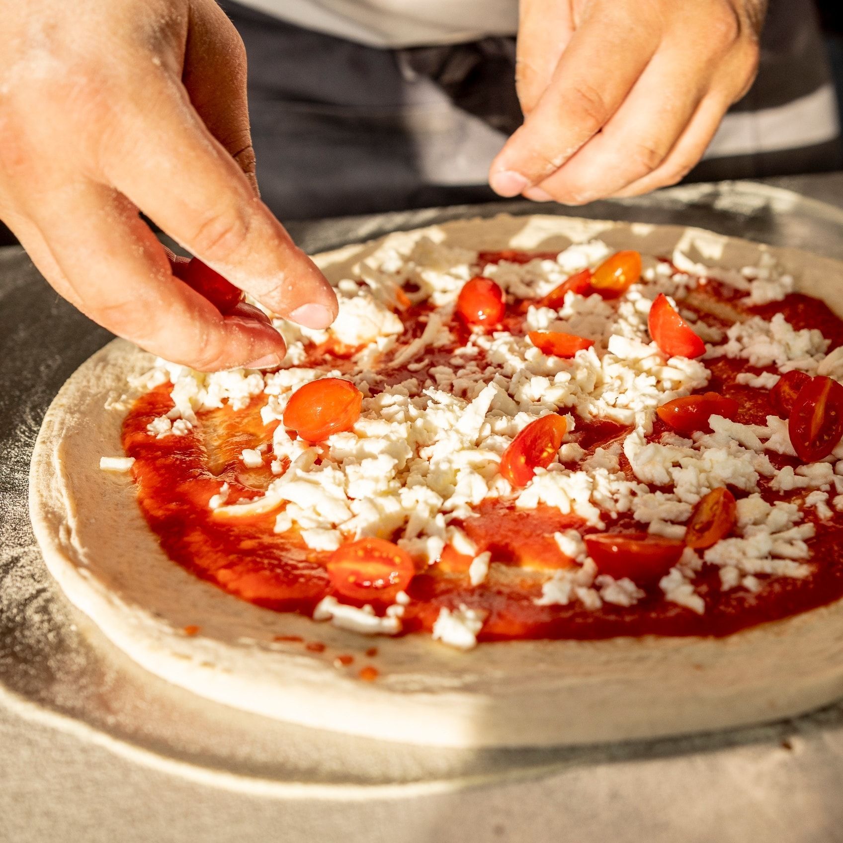 Una persona sta mettendo pomodori e formaggio su una pizza