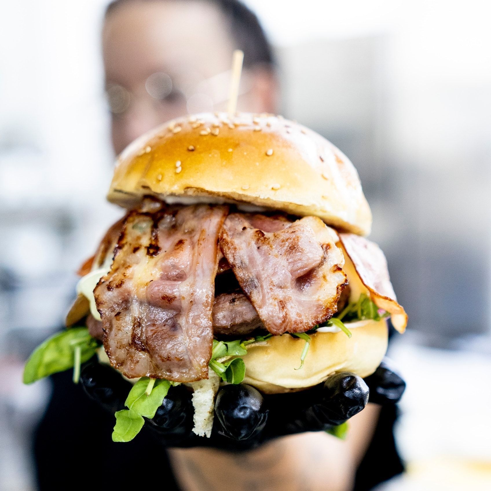 Una persona tiene in mano un hamburger con bacon e lattuga