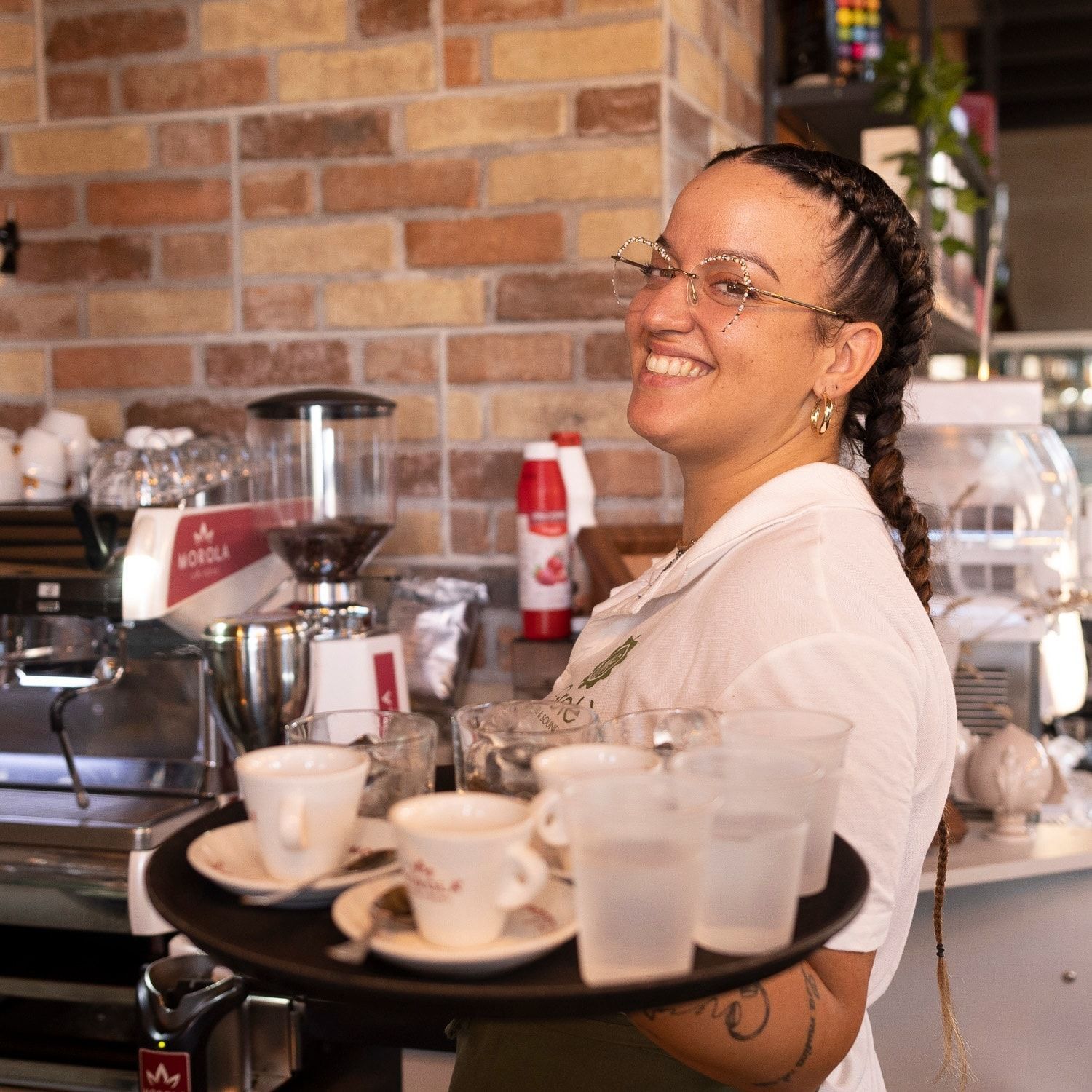 Una donna sorride mentre tiene in mano un vassoio di tazze e piattini.