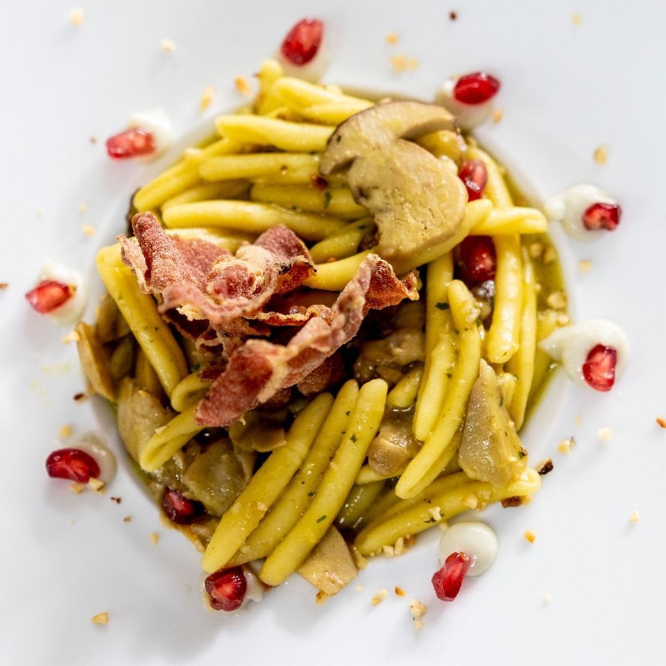 Un piatto bianco condito con pasta, pancetta, funghi e semi di melograno.