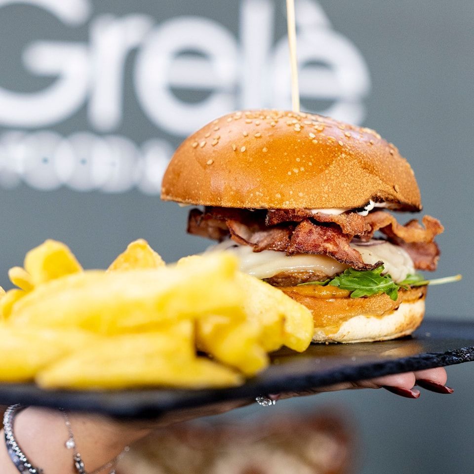 Una persona tiene in mano un piatto con un hamburger e delle patatine fritte sopra