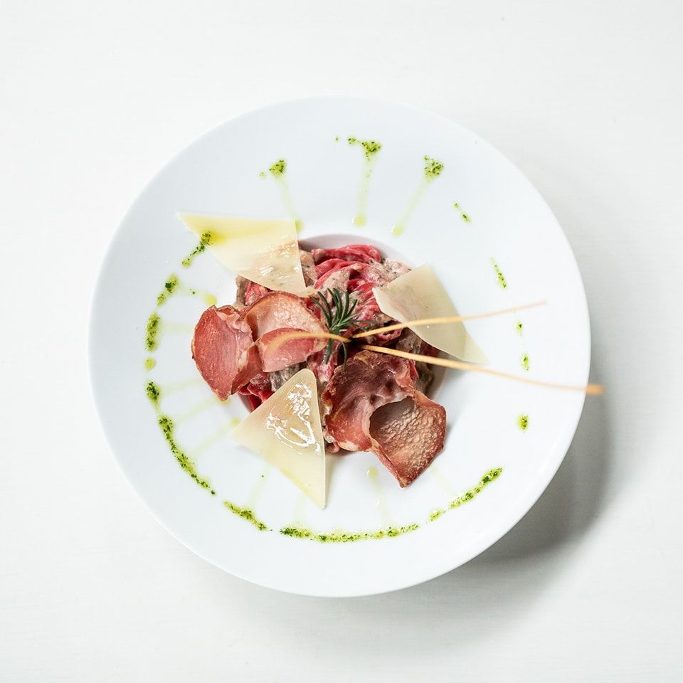 Un piatto bianco con sopra carne e formaggio su un tavolo.