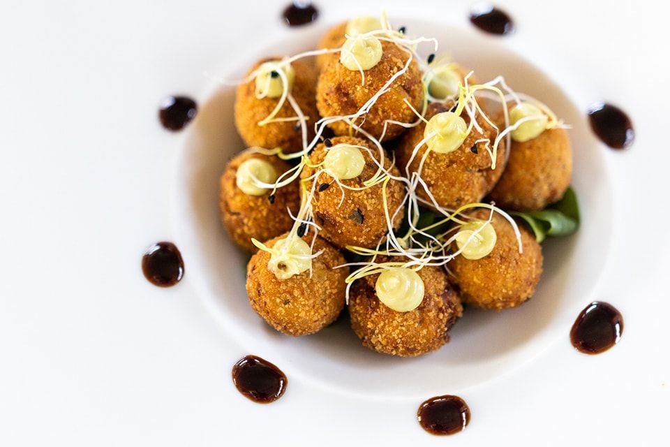 Un piatto bianco con sopra delle palline di cibo fritto e della salsa.