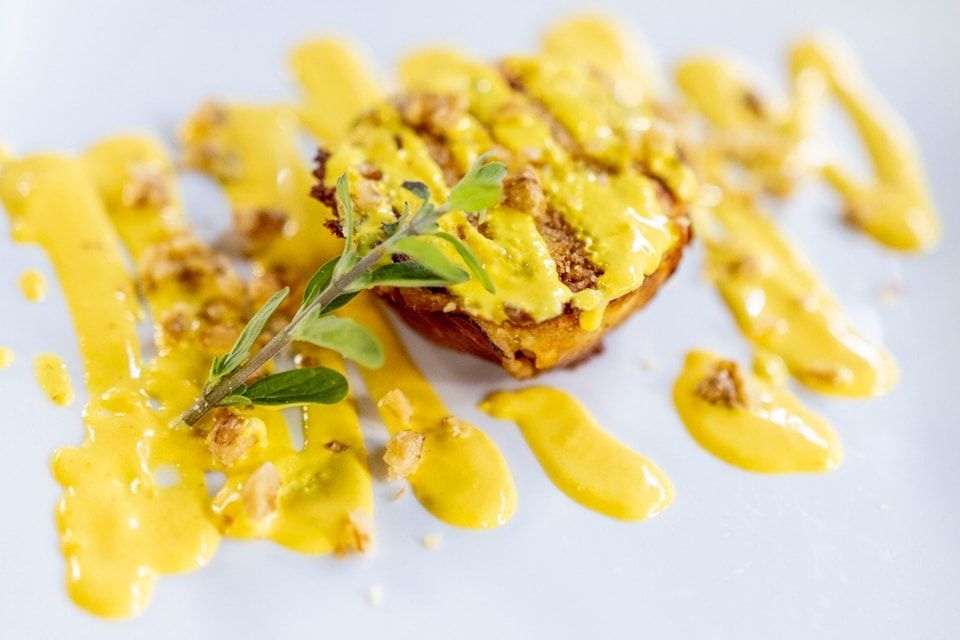 Un piatto bianco sormontato da un pezzo di cibo e da una salsa gialla.