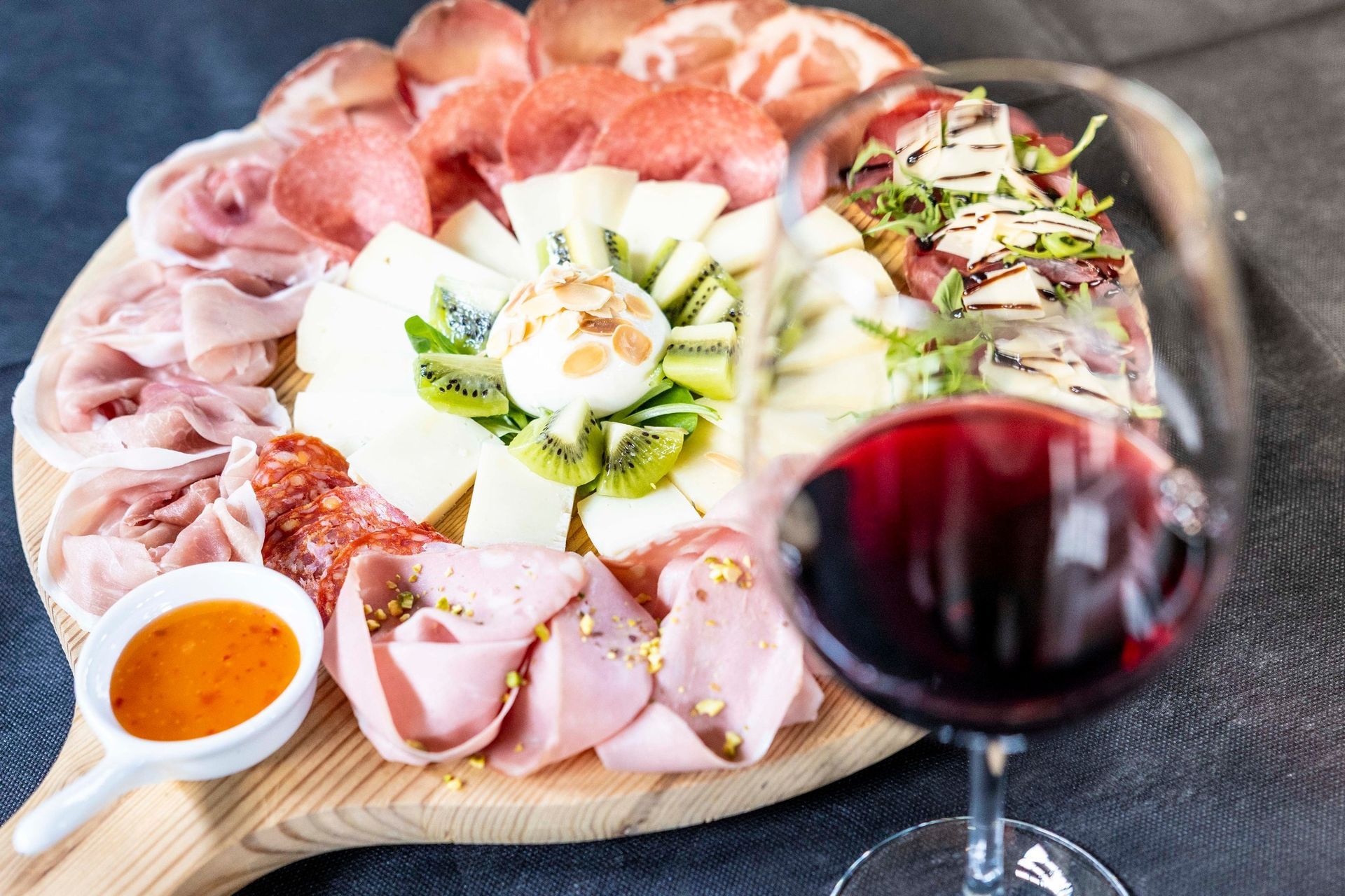 Un tagliere di legno con sopra carne e verdure accanto a un bicchiere di vino rosso.
