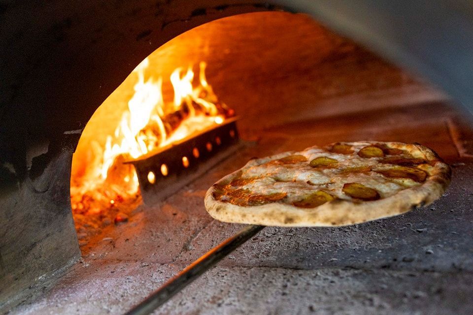 Una pizza viene cotta nel forno a legna.