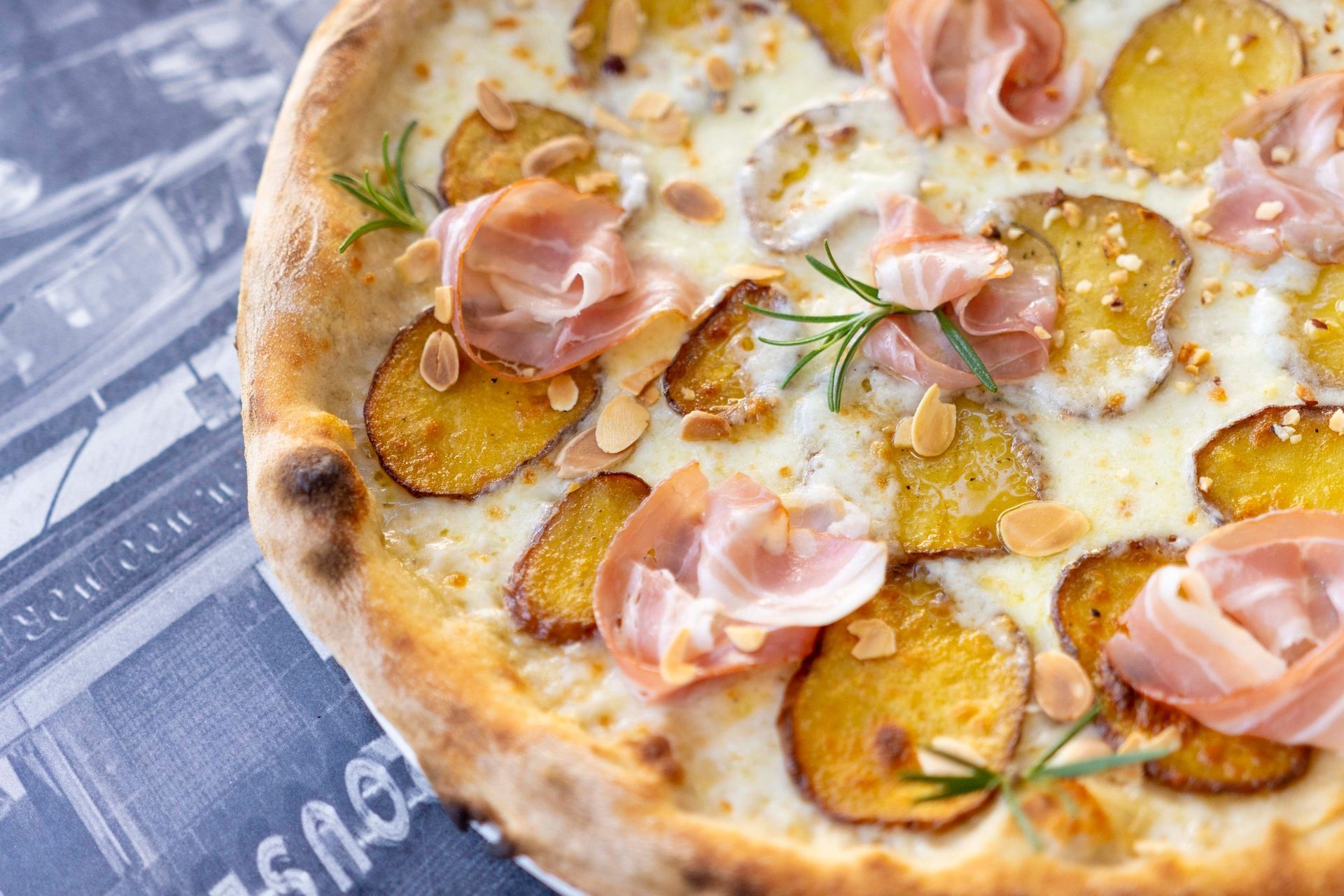 Una pizza con patate e prosciutto è appoggiata su un tavolo.