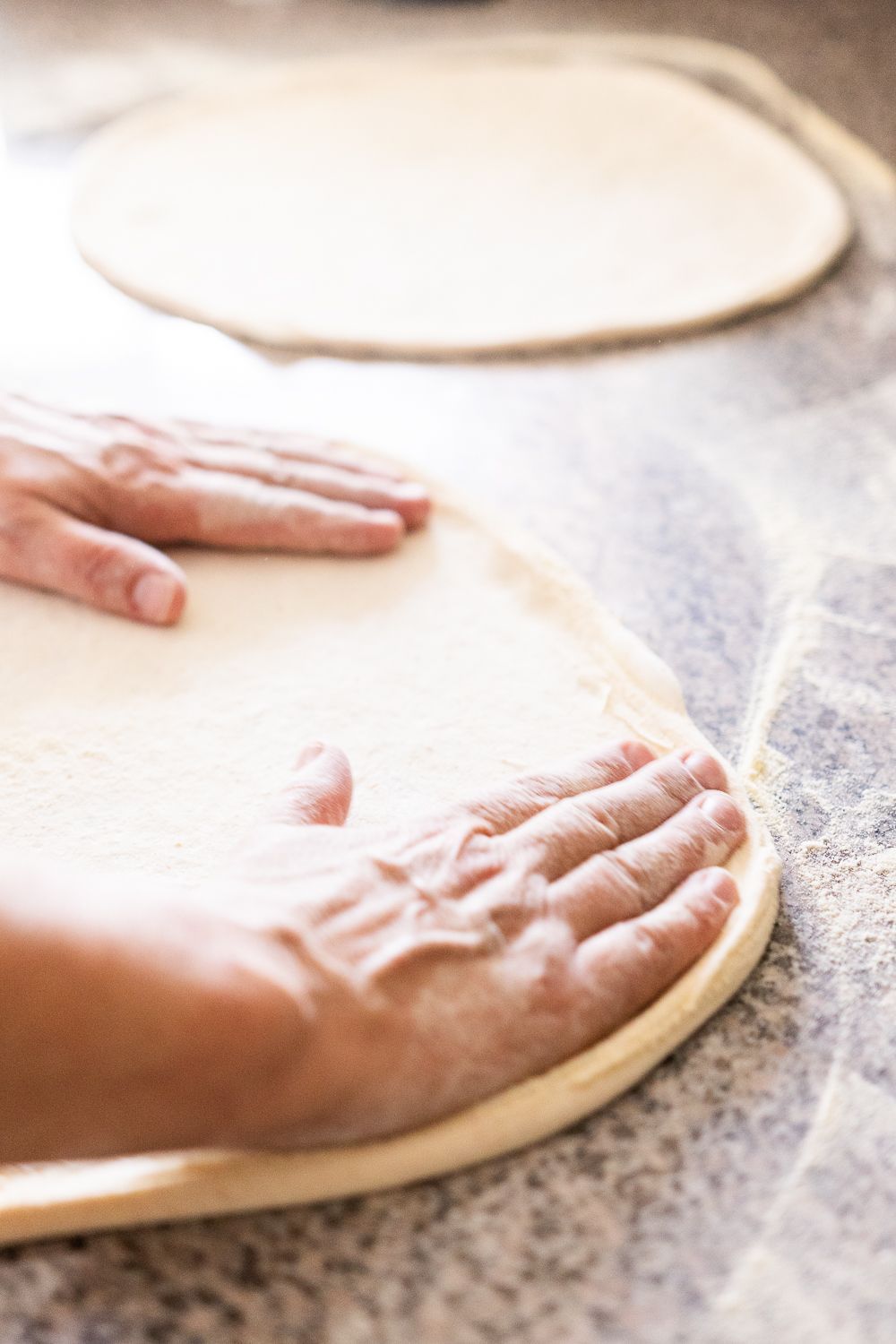 Una persona sta stendendo la pasta della pizza su un tavolo.