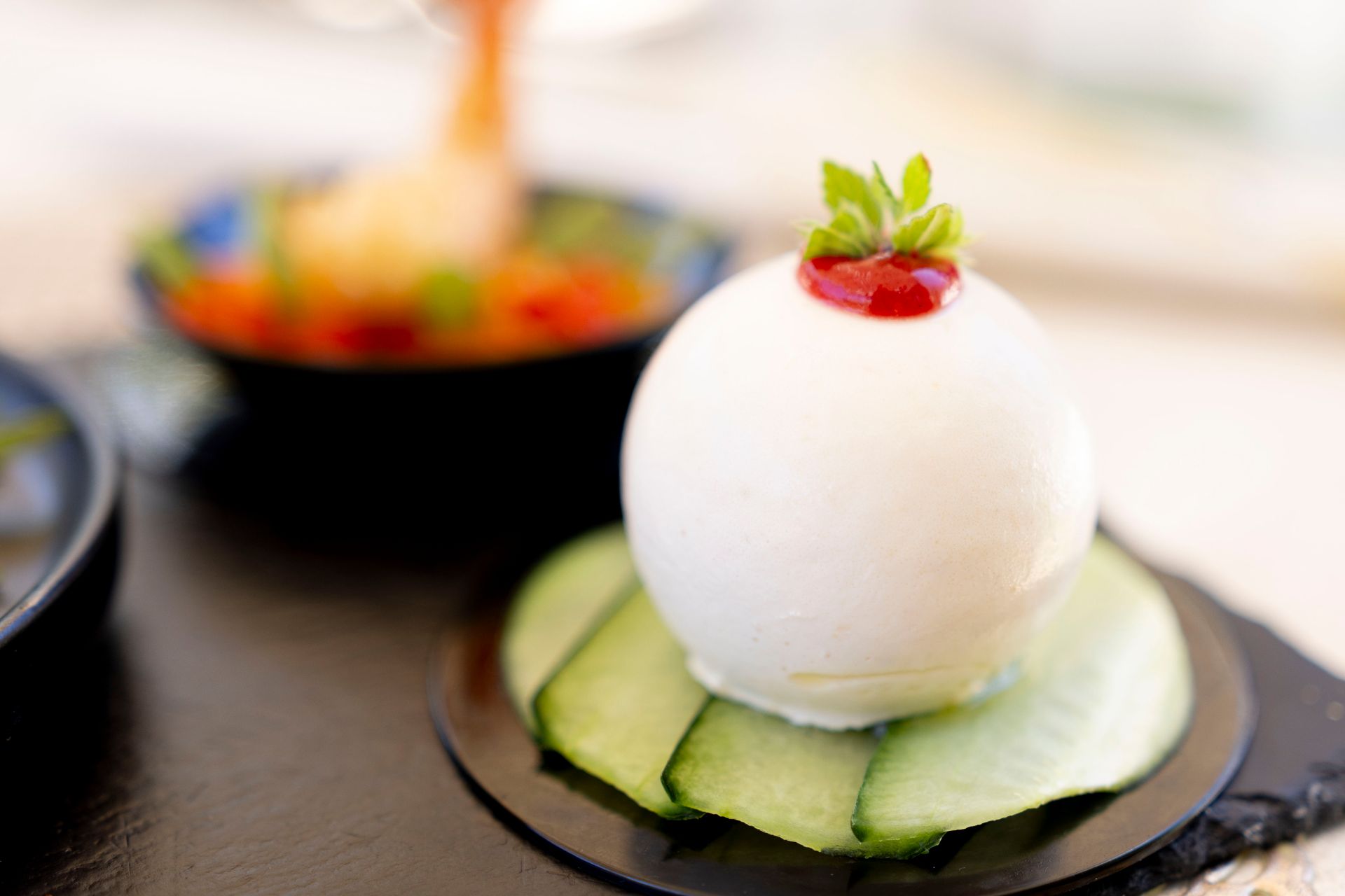 Una pallina bianca con una fragola sopra si trova su una fetta di cetriolo su un piatto.