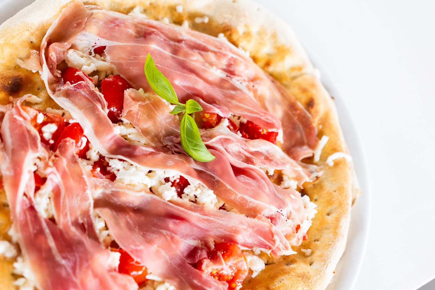 Una pizza con prosciutto, pomodori e formaggio su un piatto bianco.