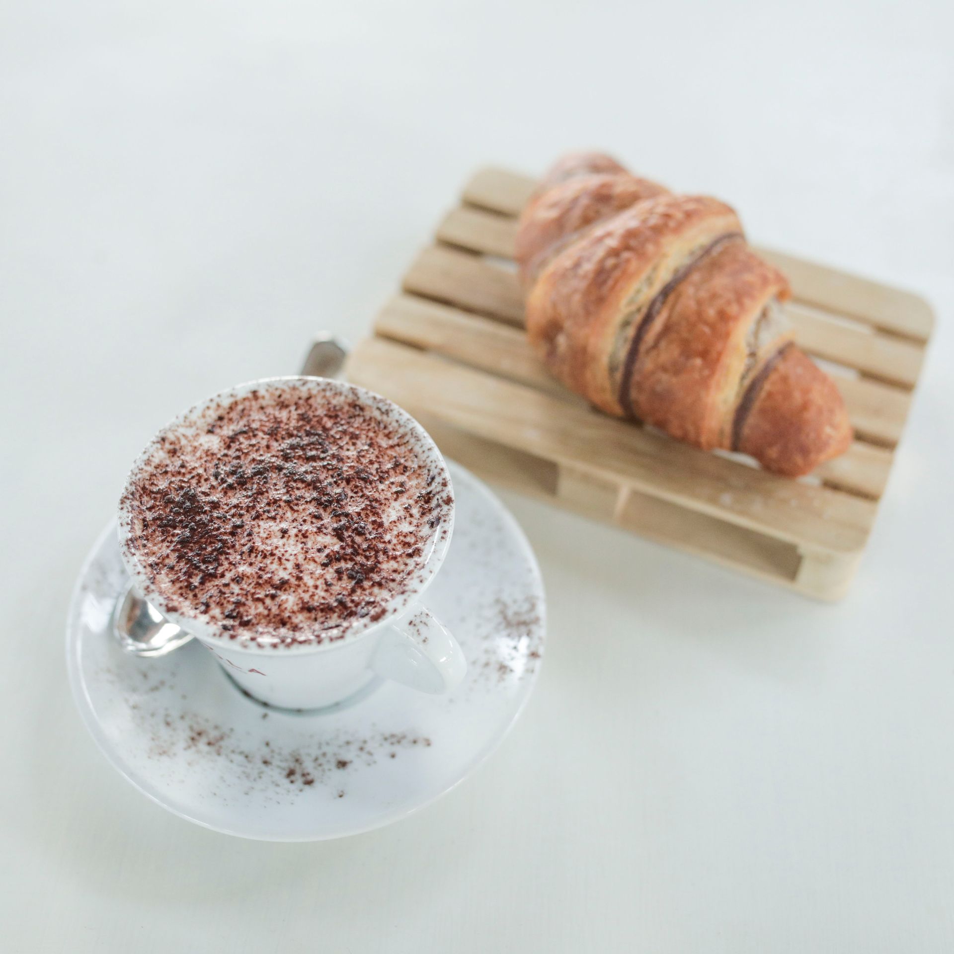 Una tazza di caffè e un croissant su un vassoio di legno su un tavolo.