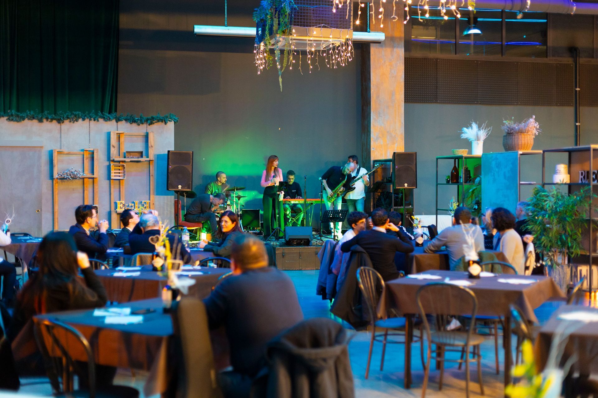 Un gruppo di persone è seduto ai tavoli di un ristorante e guarda una band sul palco.