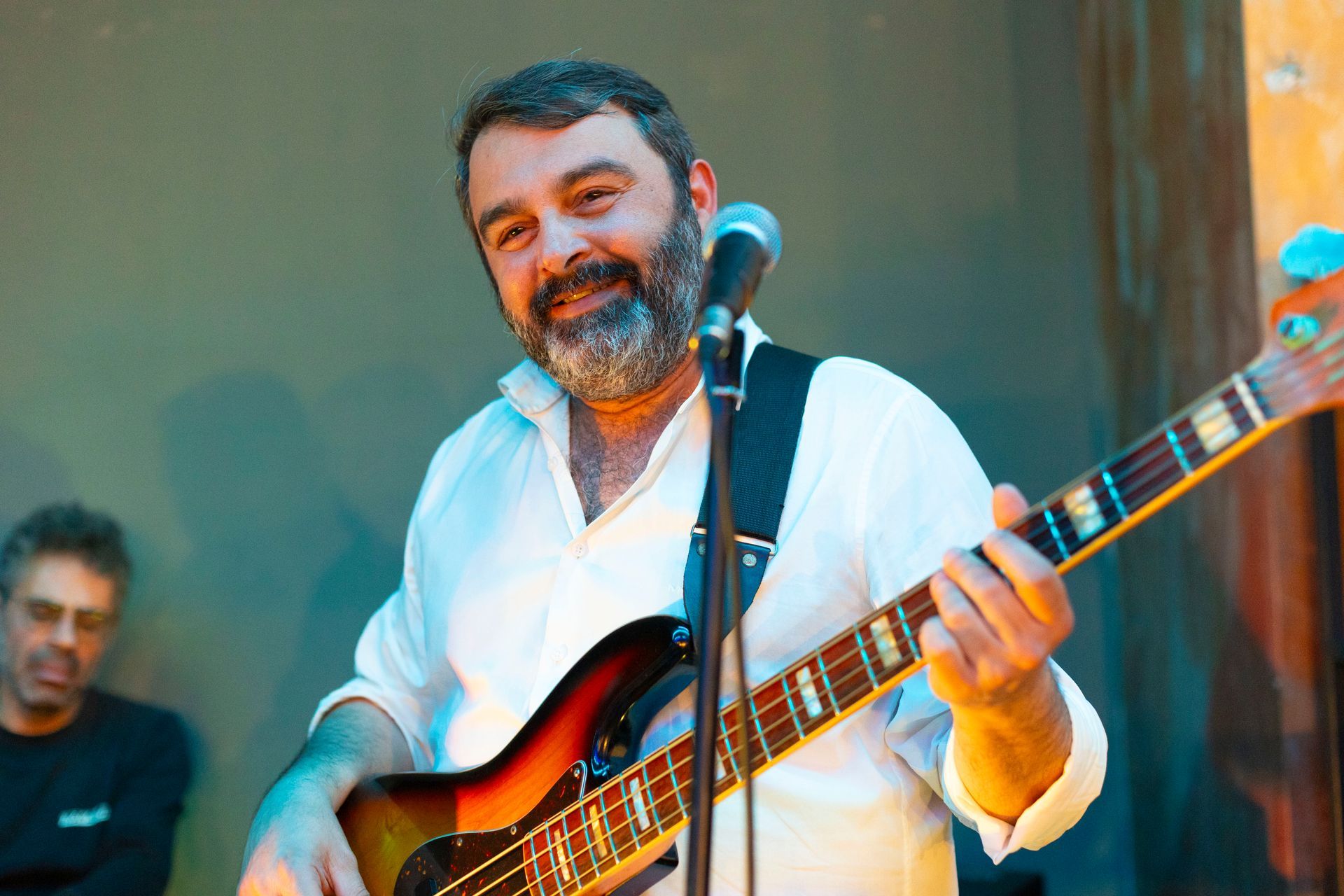 Un uomo con la barba suona la chitarra e canta in un microfono.