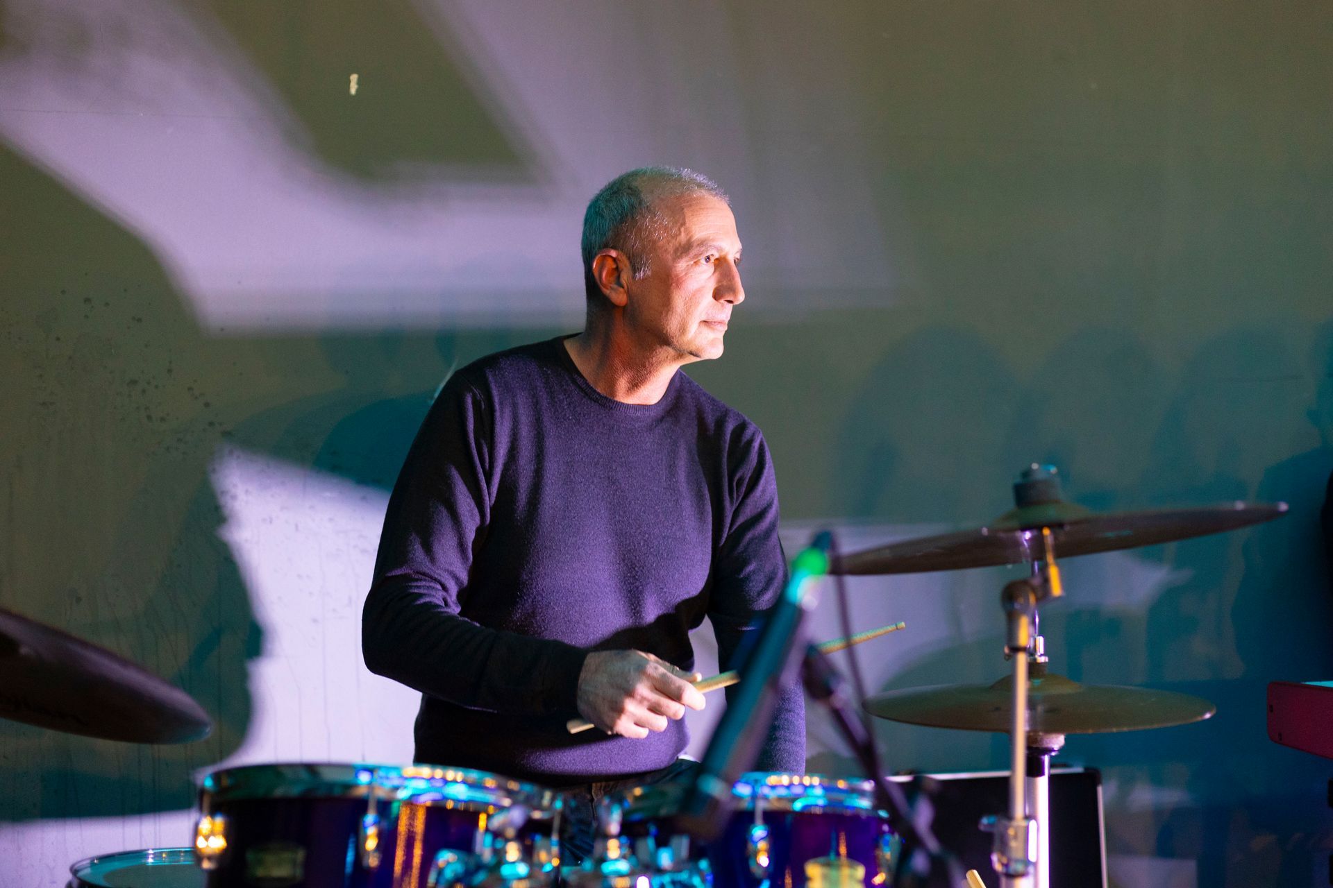 Un uomo suona la batteria su un palco in una stanza buia.