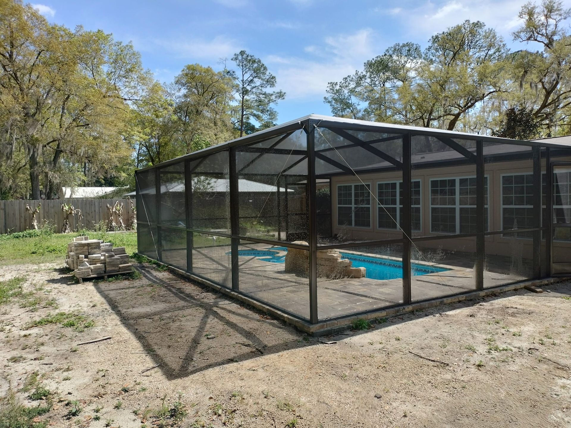 A screened in swimming pool in the backyard of a house.