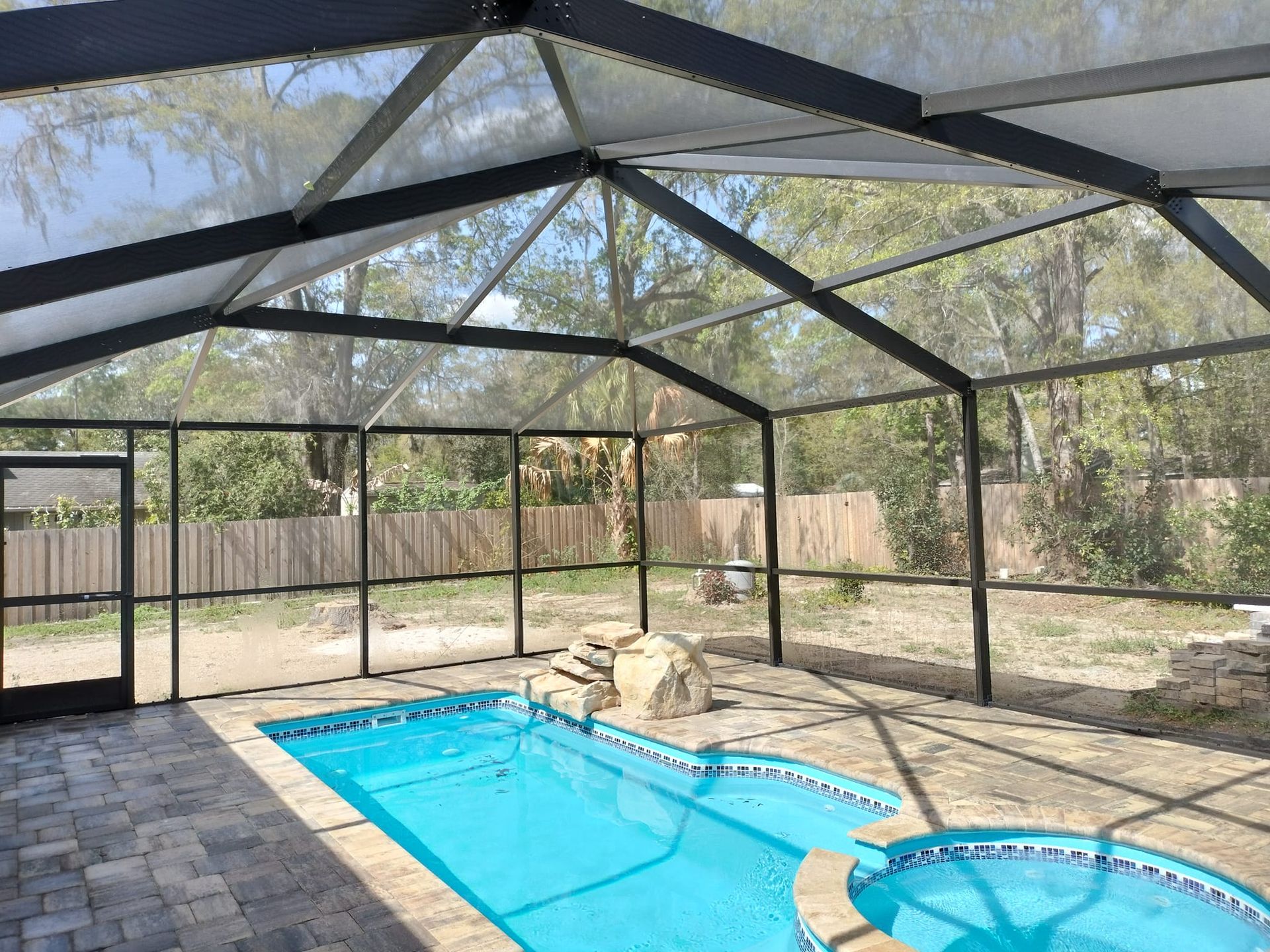 There is a swimming pool inside of a screened in area.
