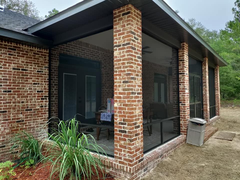 A brick house with a screened in porch with a lot of windows.