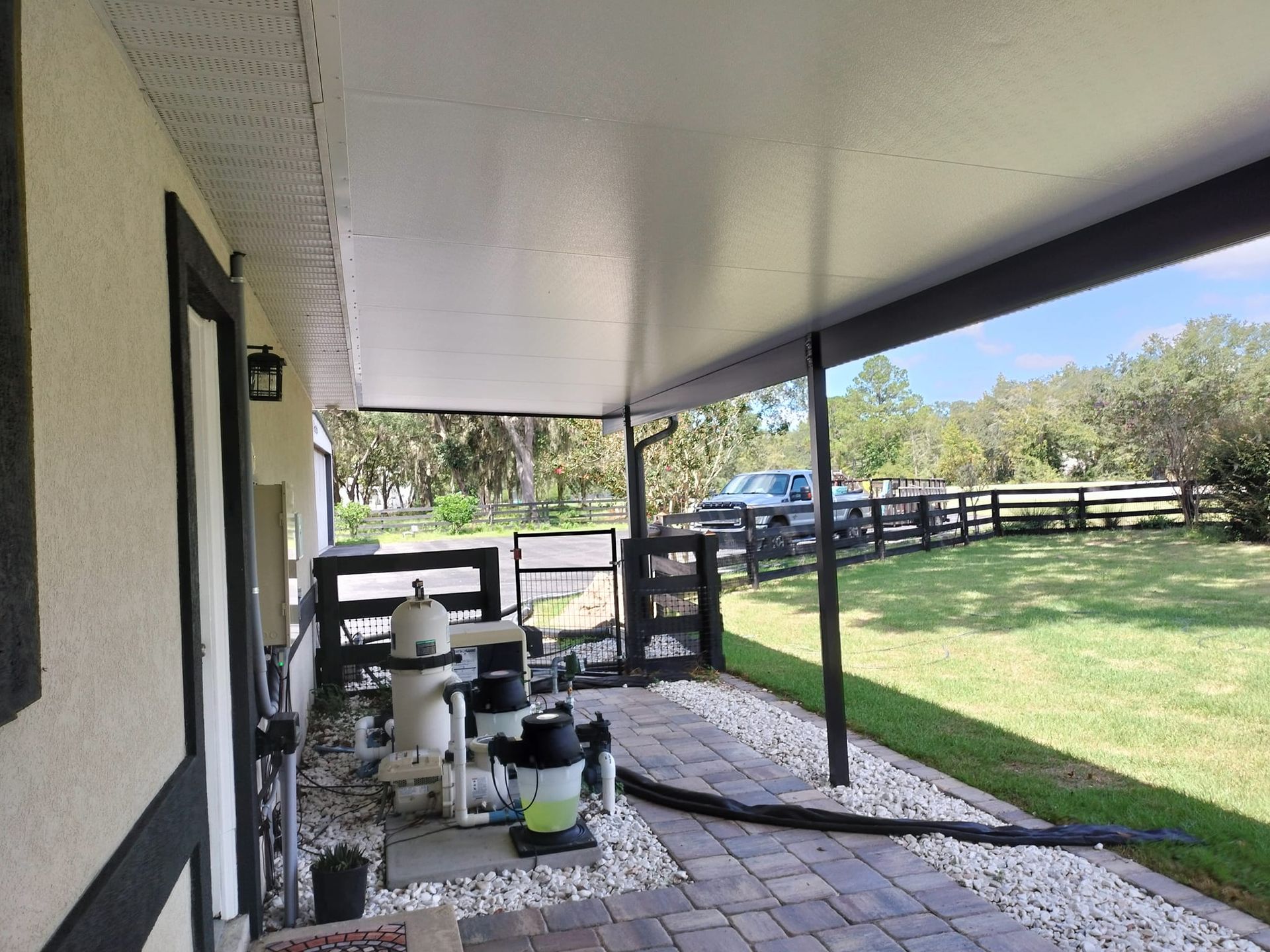 A covered patio with a pool filter and a fence in the background.