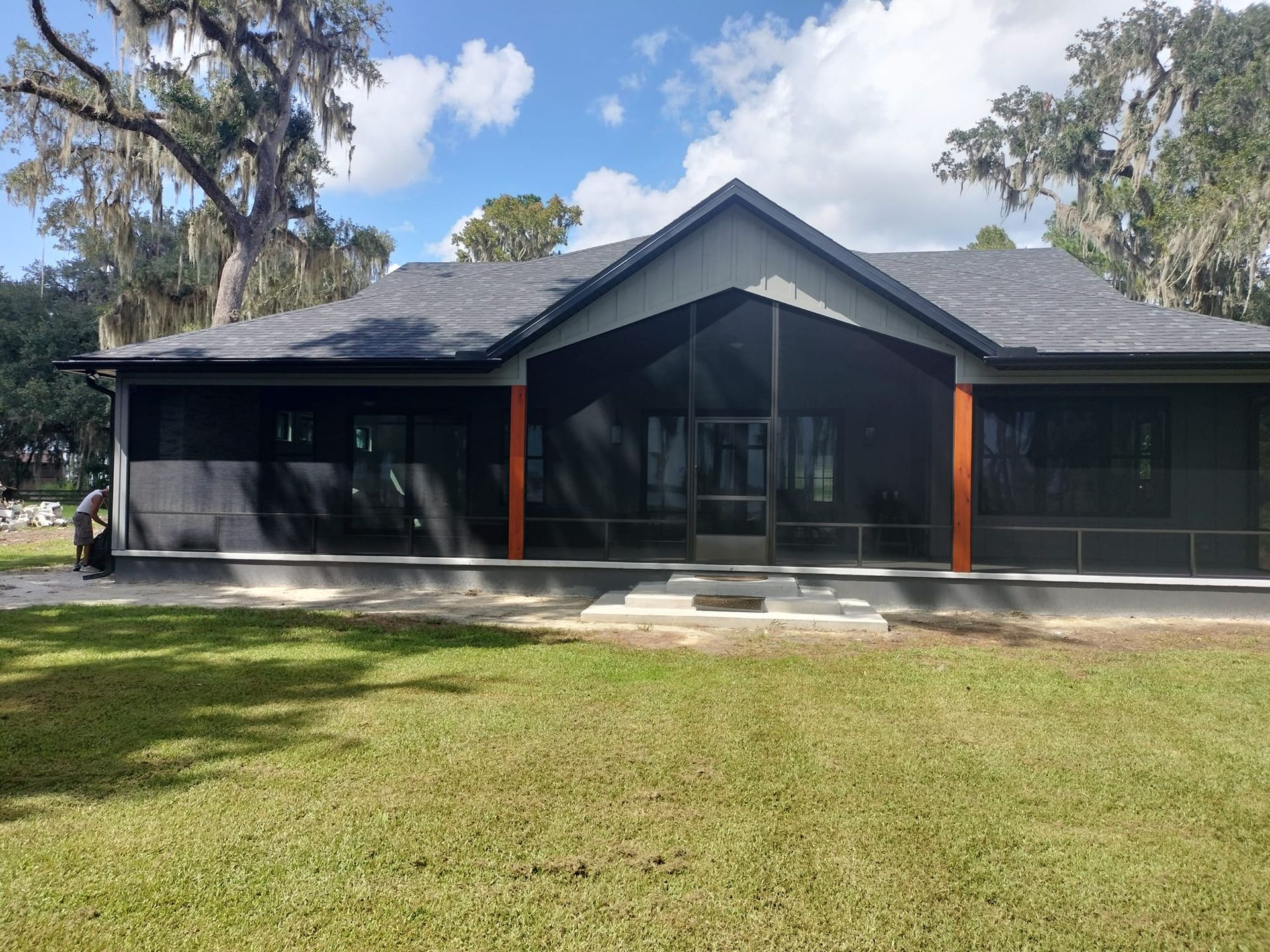 A house with a screened in porch and a large lawn in front of it.