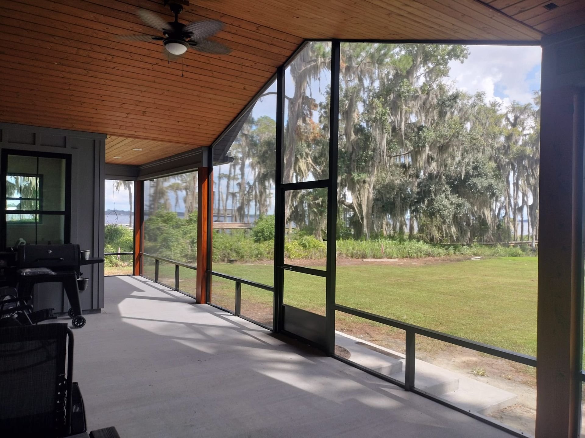 A screened in porch with a ceiling fan and a view of a field.