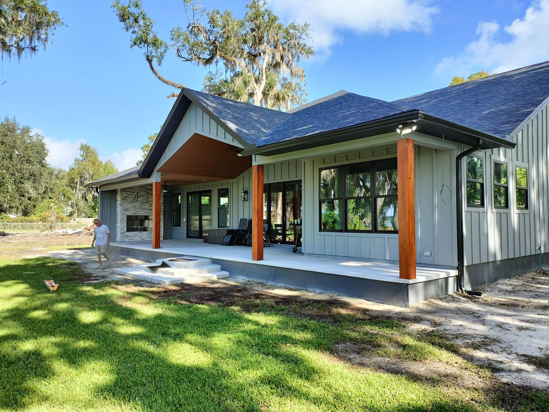 A man is standing in front of a large house with a blue roof.