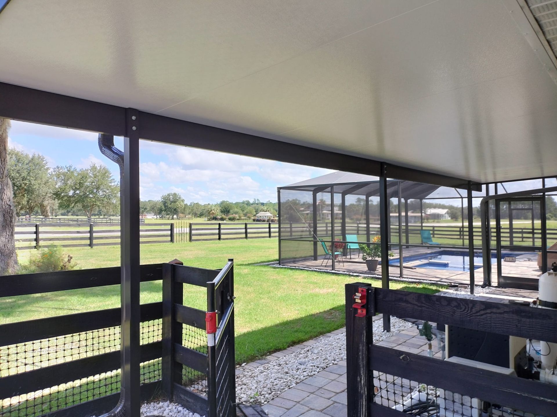 A covered patio with a fence and a pool in the background