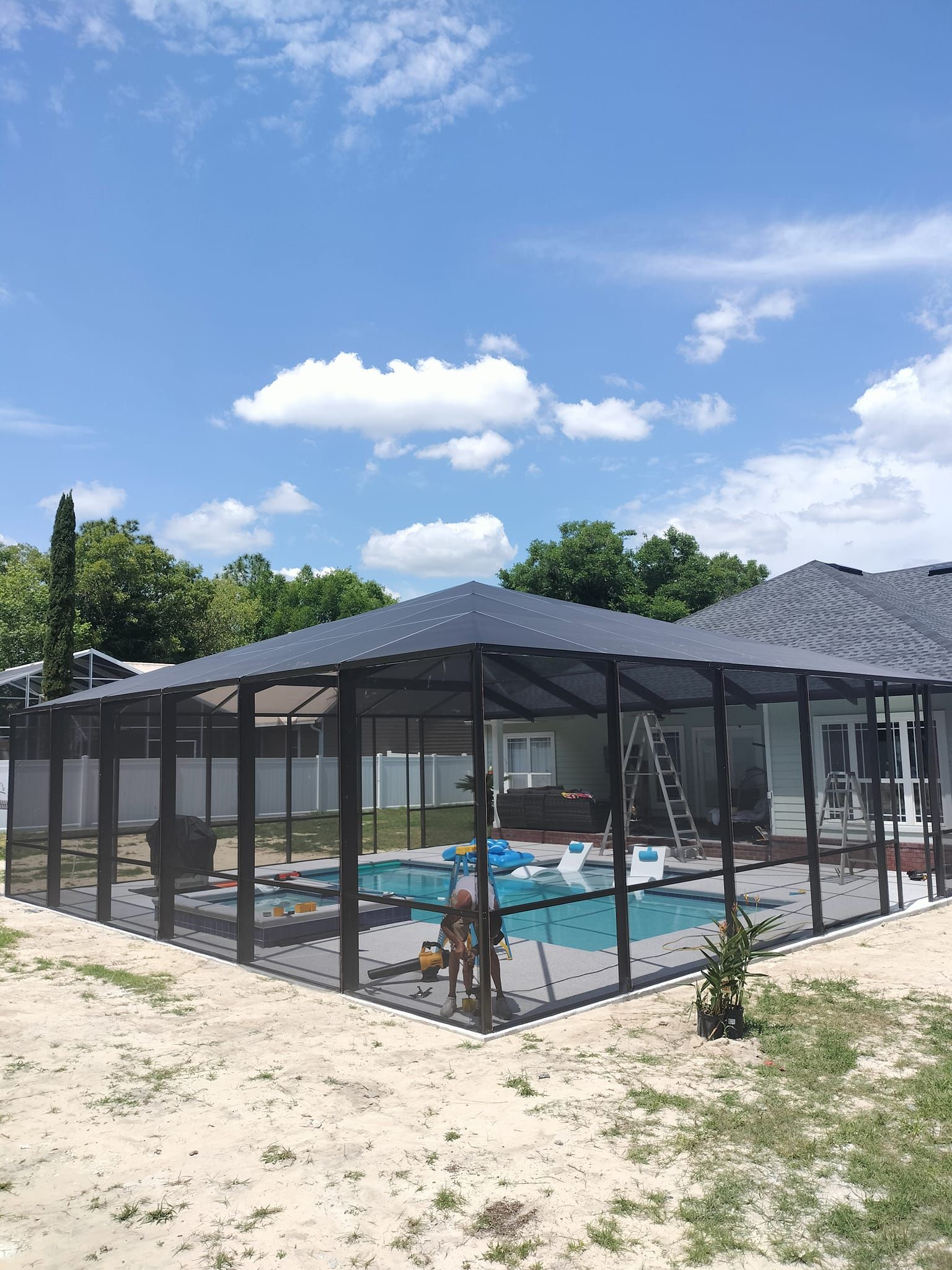 A screened in swimming pool with a canopy over it and a house in the background.