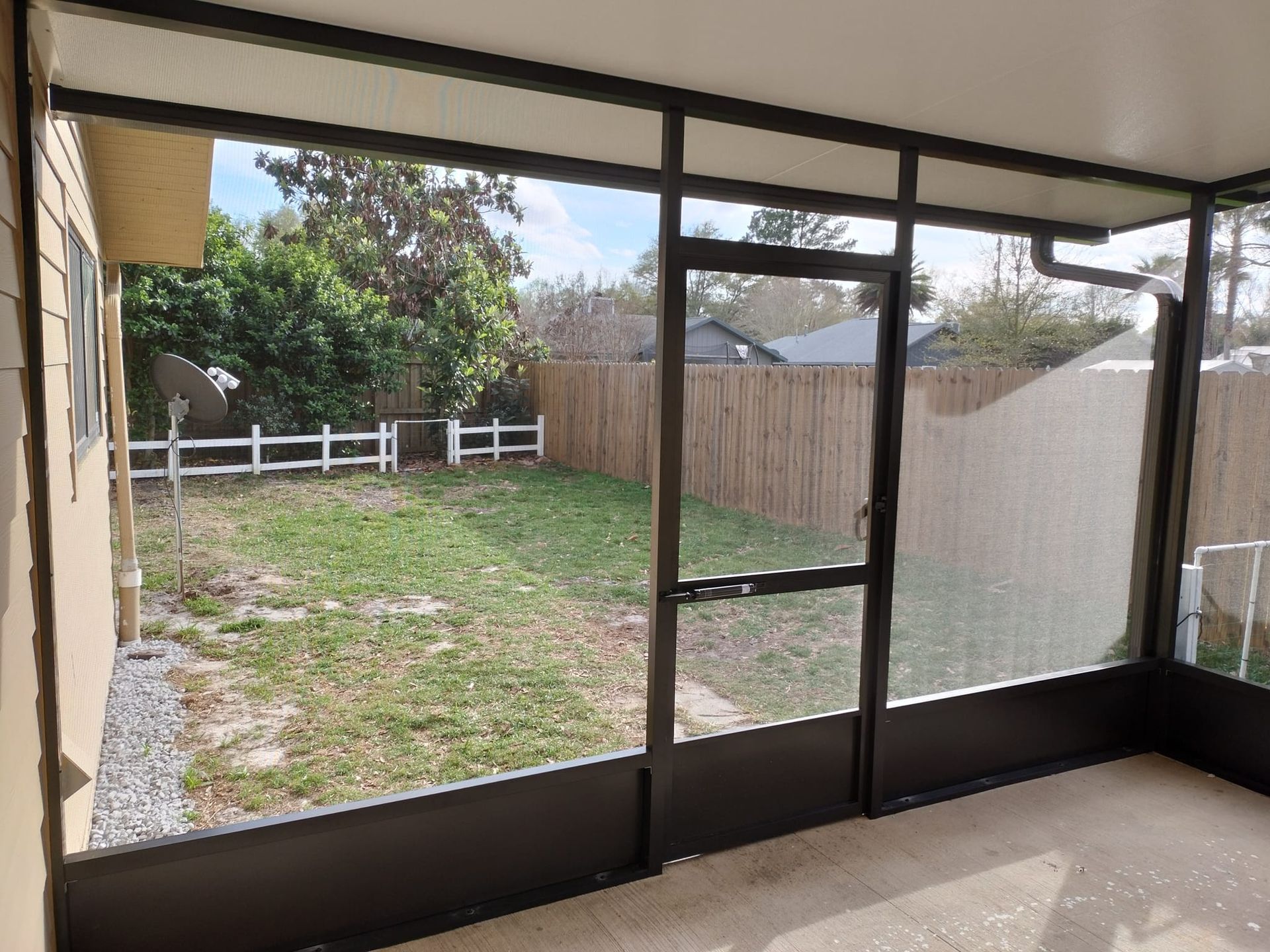A screened in porch with a view of a backyard and a fence.