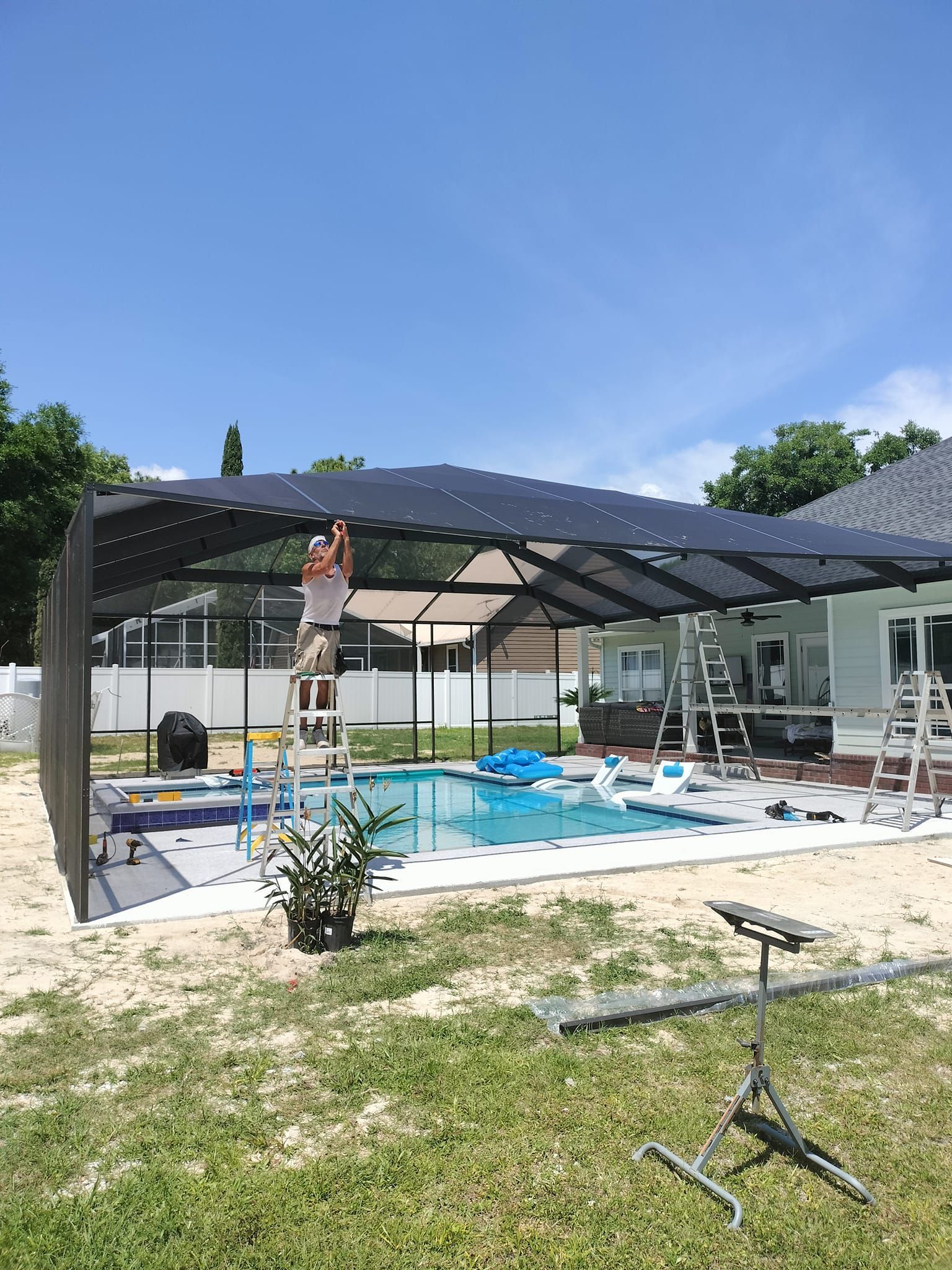 A man is standing on a ladder in front of a swimming pool.