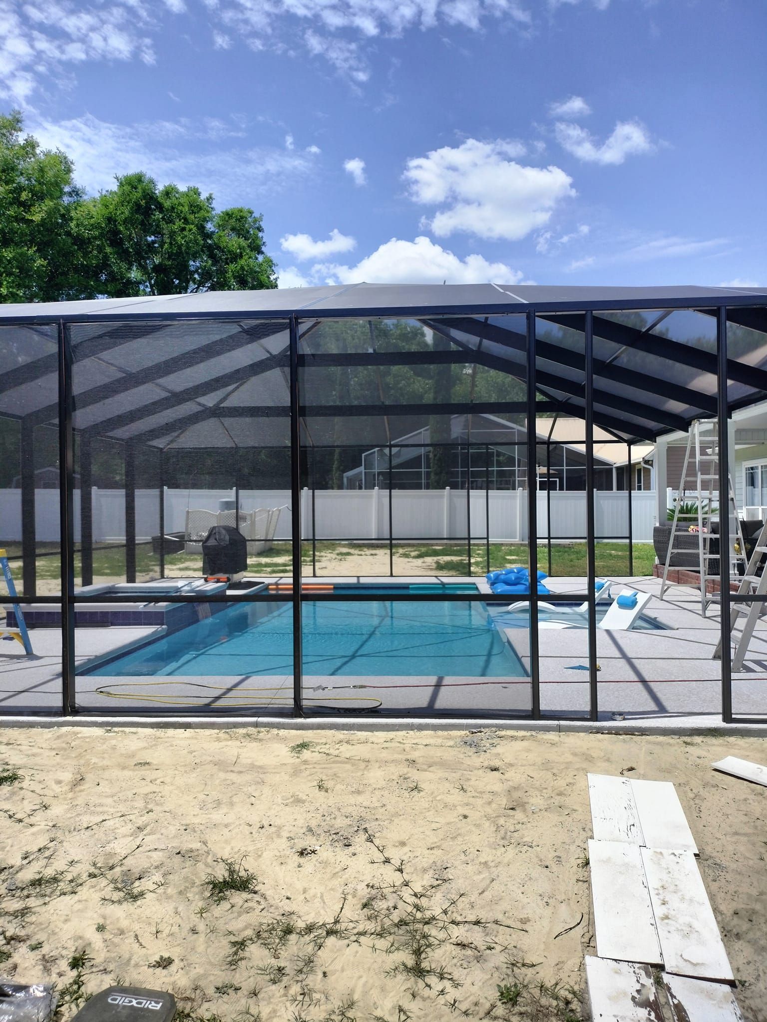 A swimming pool is behind a screened in area in a backyard.