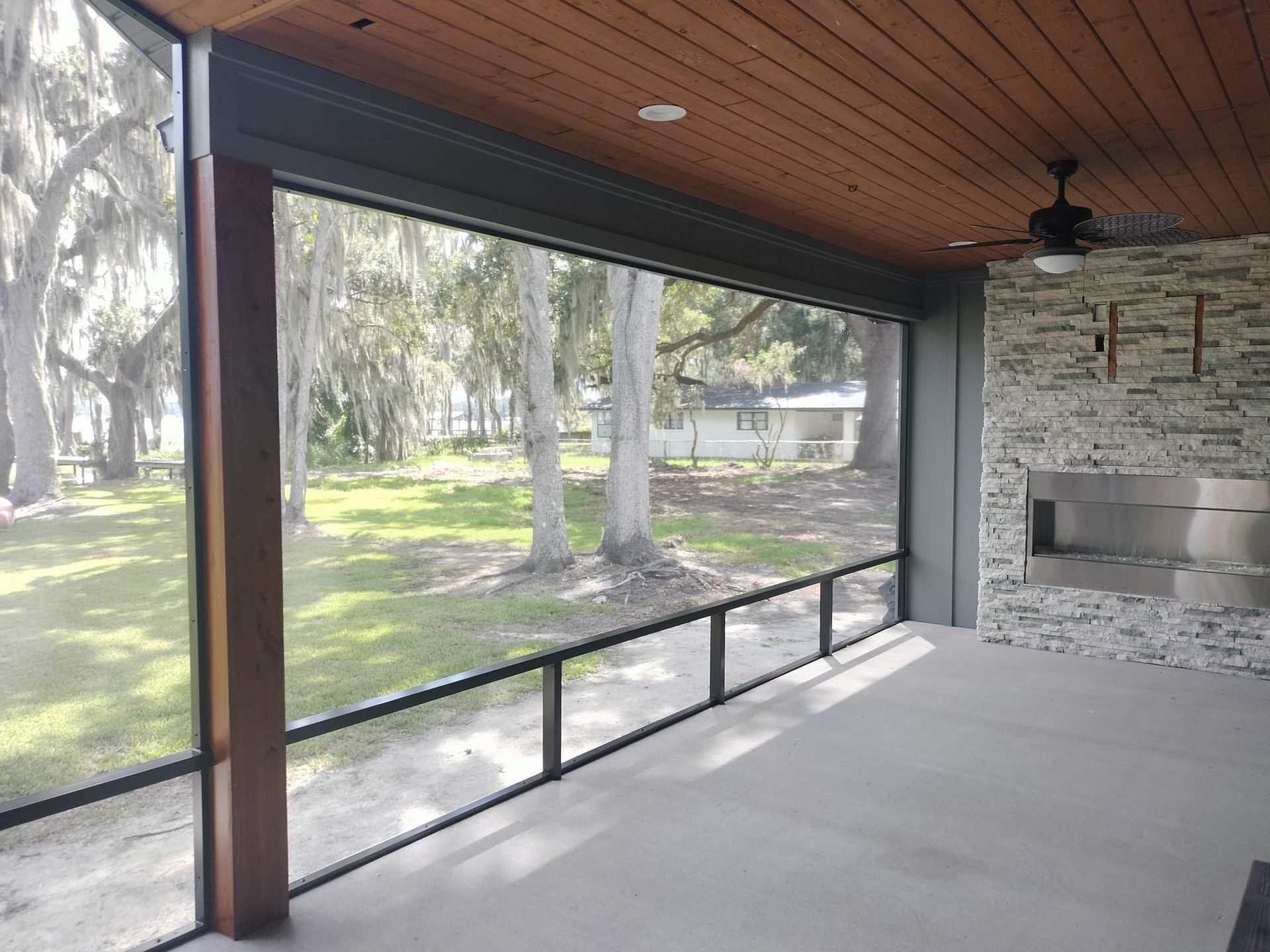 A screened in porch with a fireplace and trees in the background.