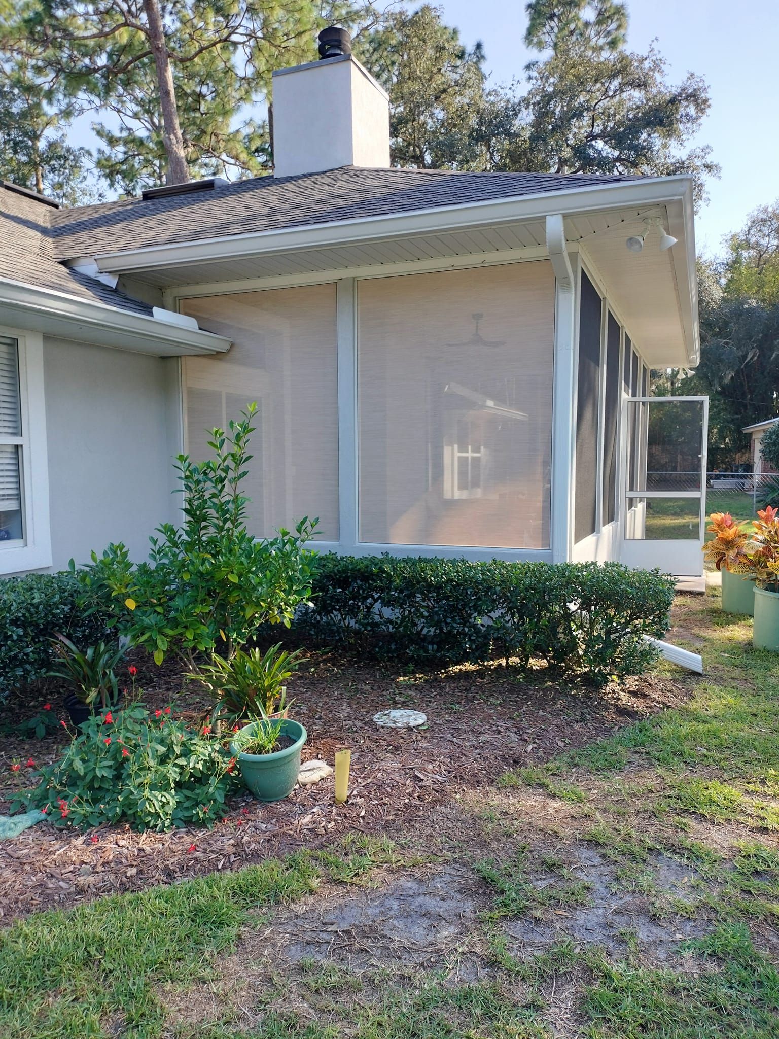 A house with a screened in porch and potted plants in front of it.
