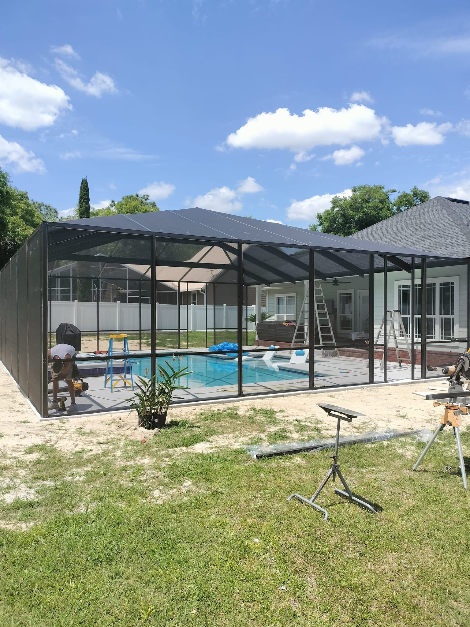 A screened in swimming pool is being built in the backyard of a house.