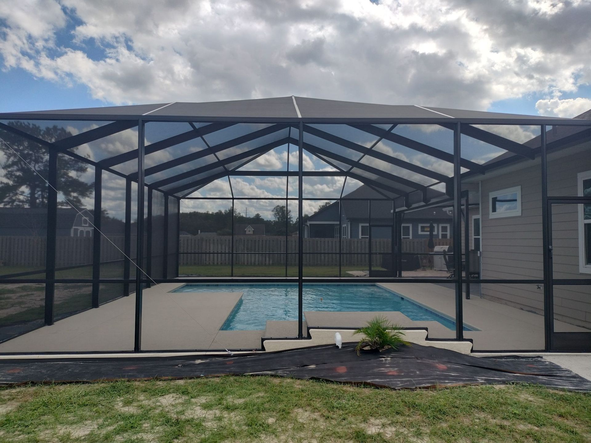 A screened in swimming pool with a house in the background.
