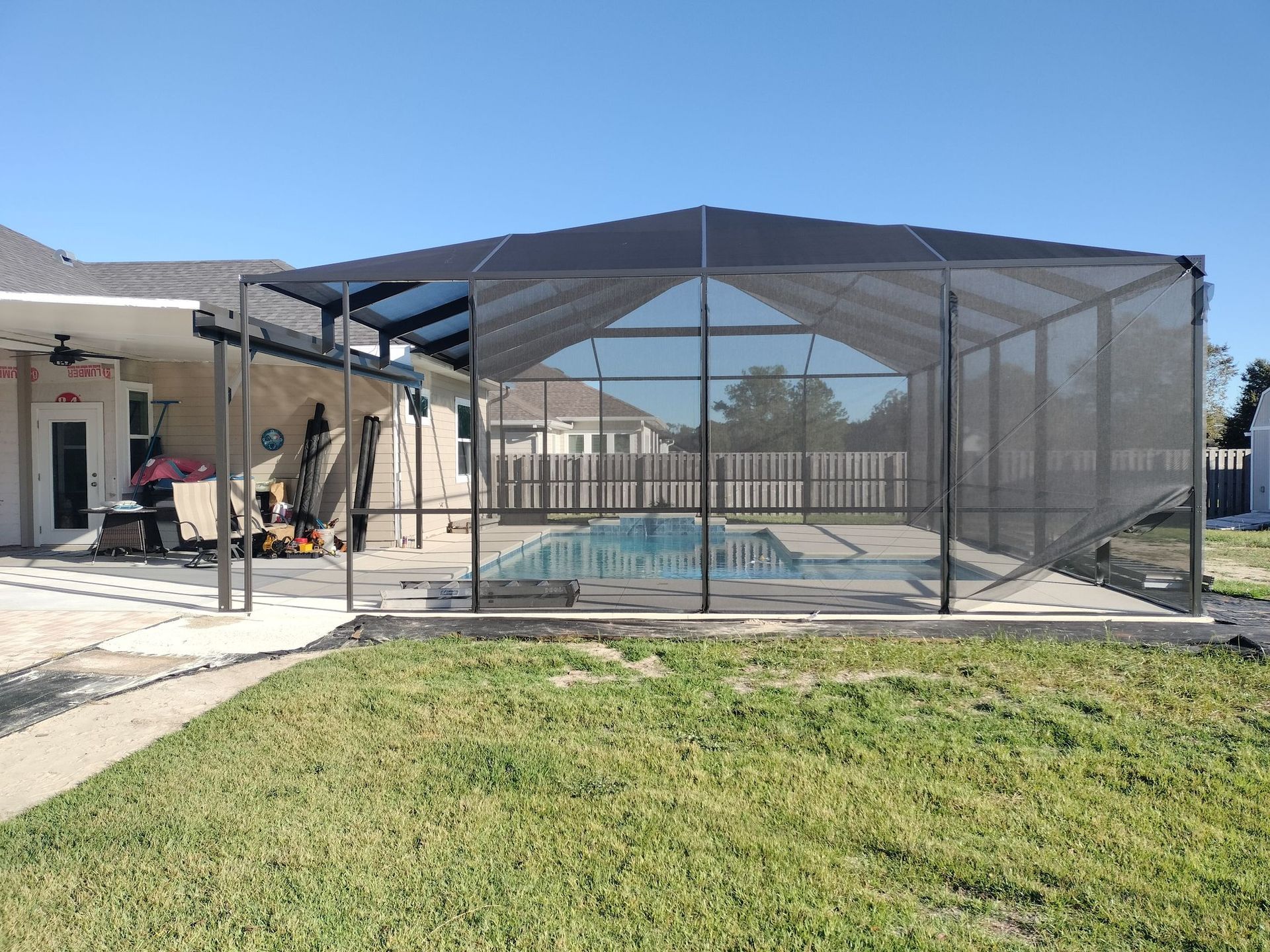 A screened in swimming pool with a house in the background.