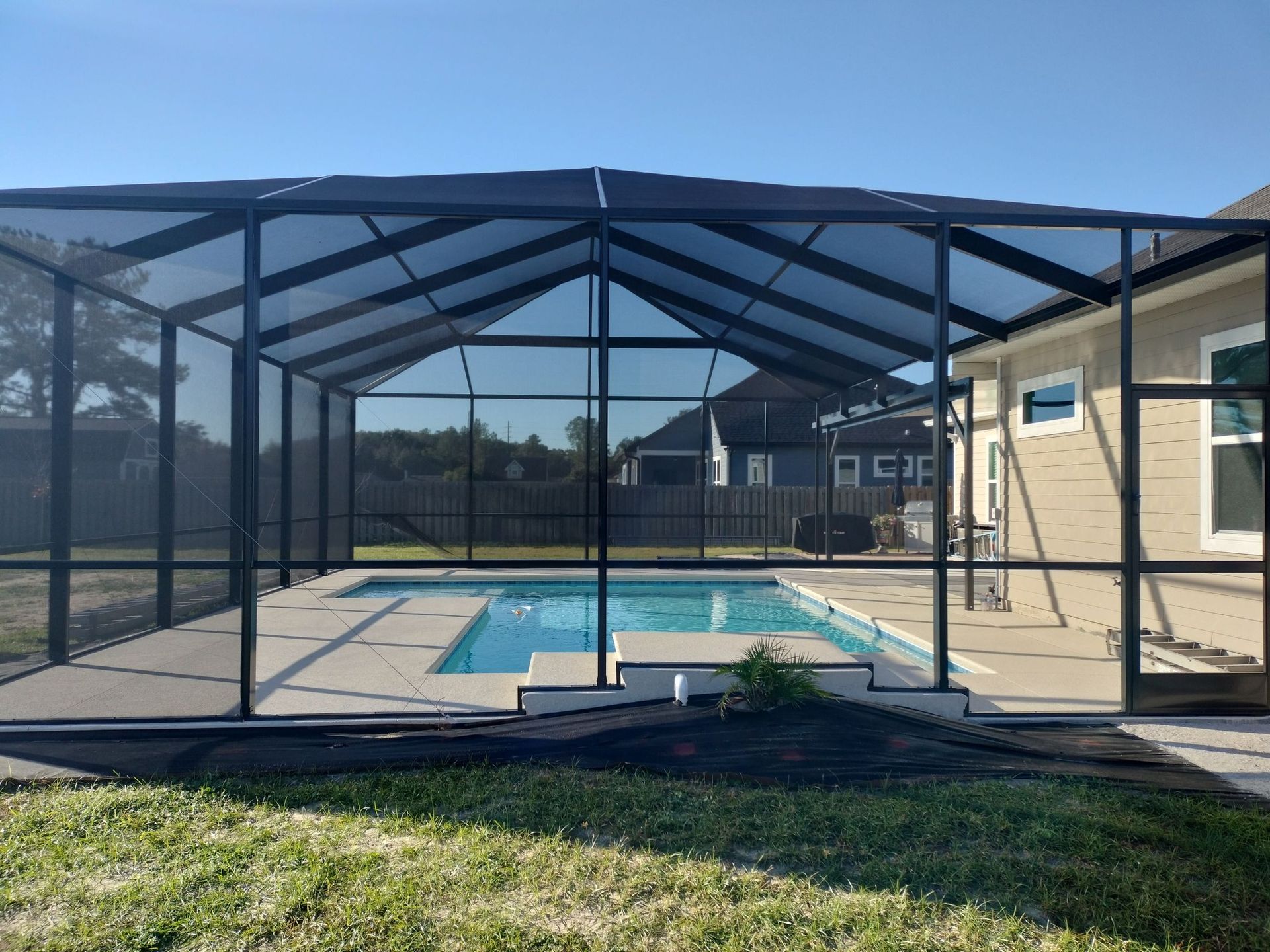 A screened in swimming pool with a house in the background.