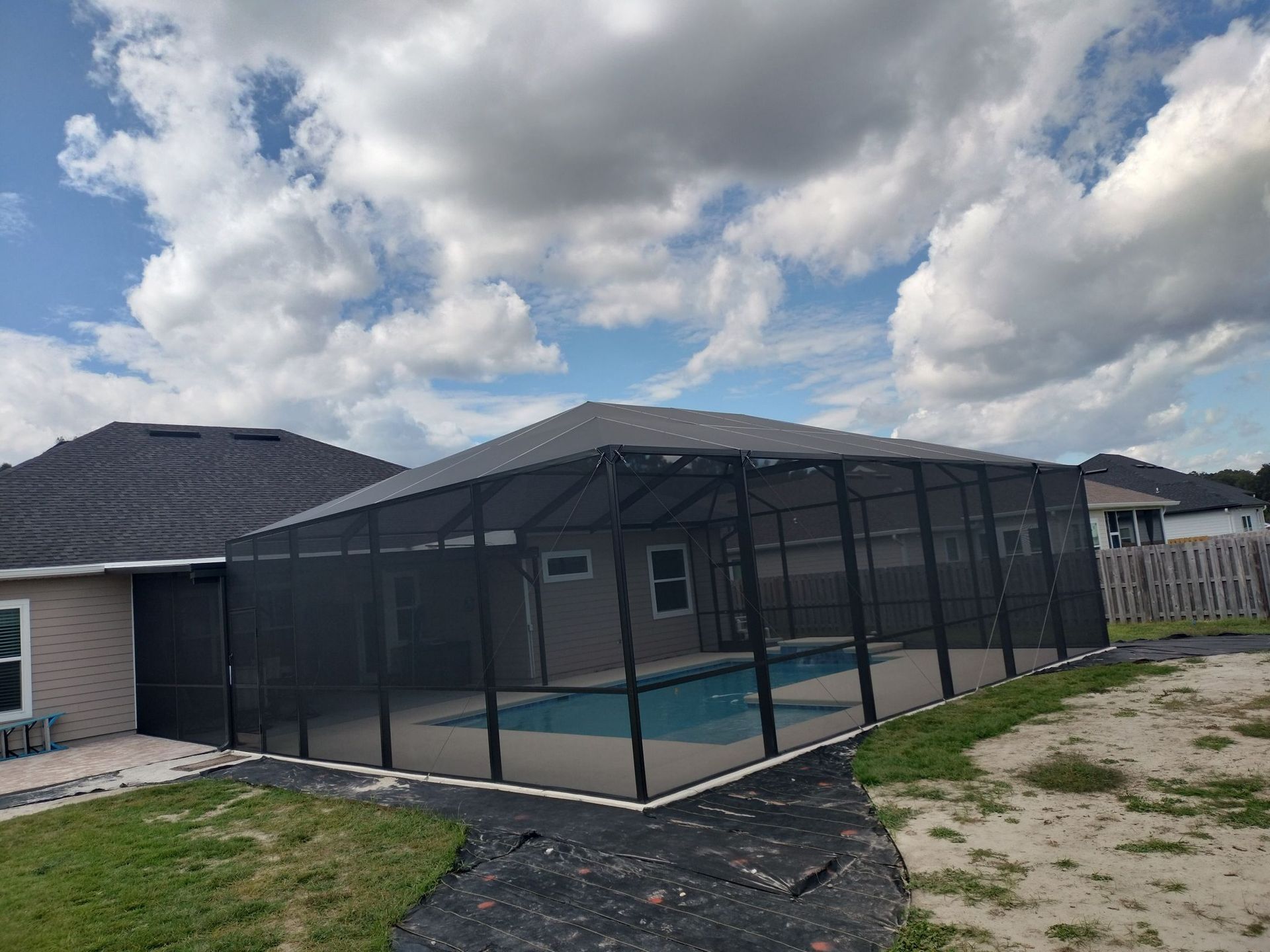 A screened in swimming pool in the backyard of a house.