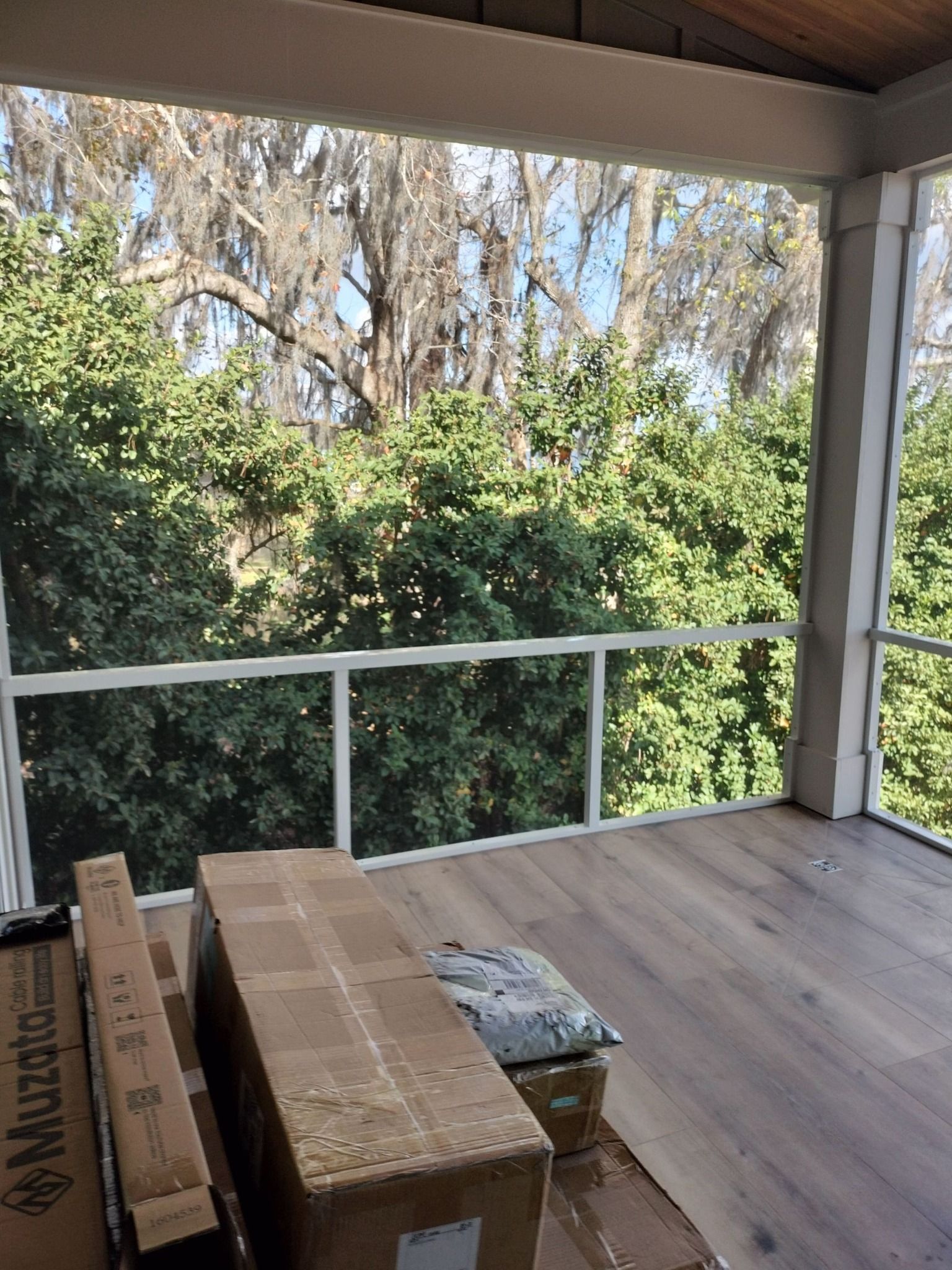 A screened in porch with boxes on the floor and trees in the background.
