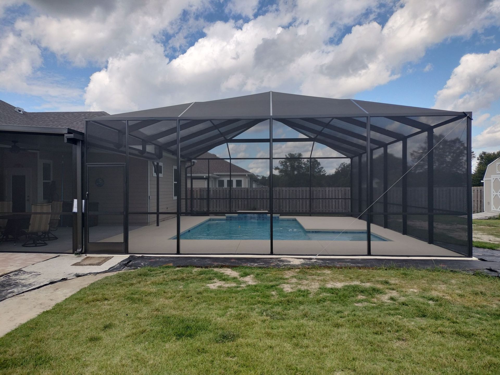 A screened in swimming pool in the backyard of a house.