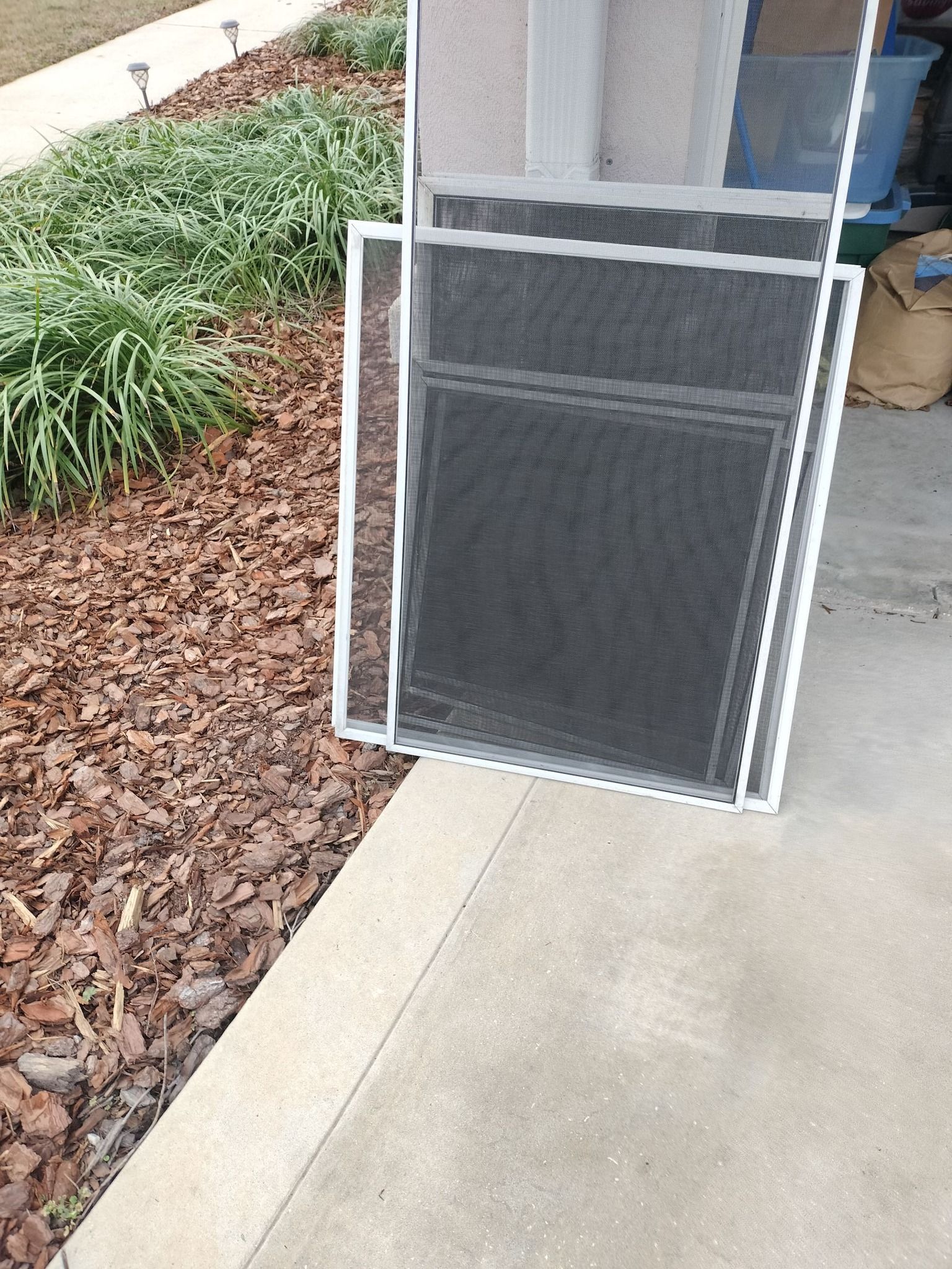 A screen door is sitting on a sidewalk next to a garden.